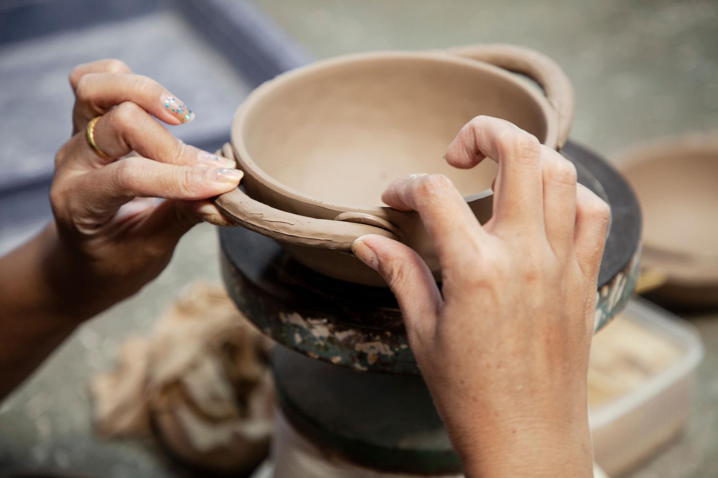 A pair of hands form the handles on a clay vase.