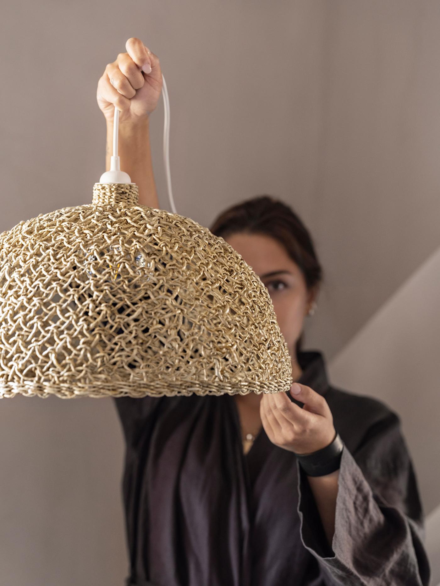 A person holds a banana fibre pendant lamp up. It obstructs part of their face.