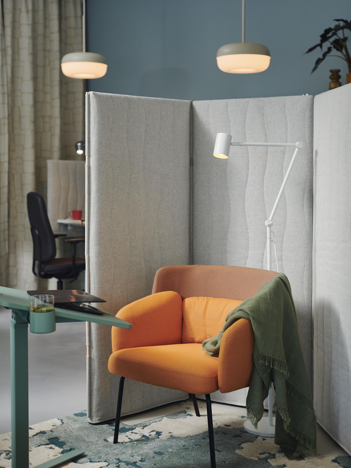 Office setting, orange chair with green plaid, green desk with laptop and a desk and black chair in the background.
