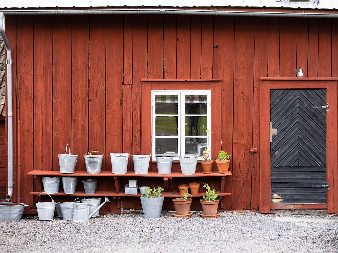 On the wall outside a shed, red-painted shelves hold buckets and plant pots.