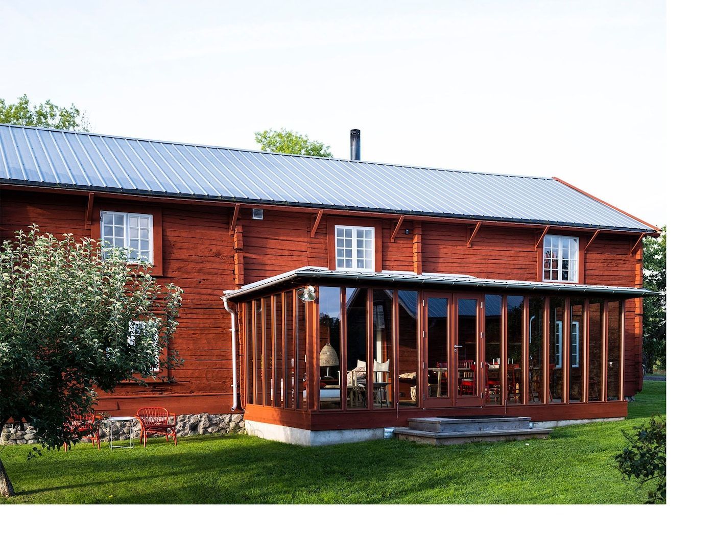 View of a Swedish farmhouse with glass sunroom looking over lawn.