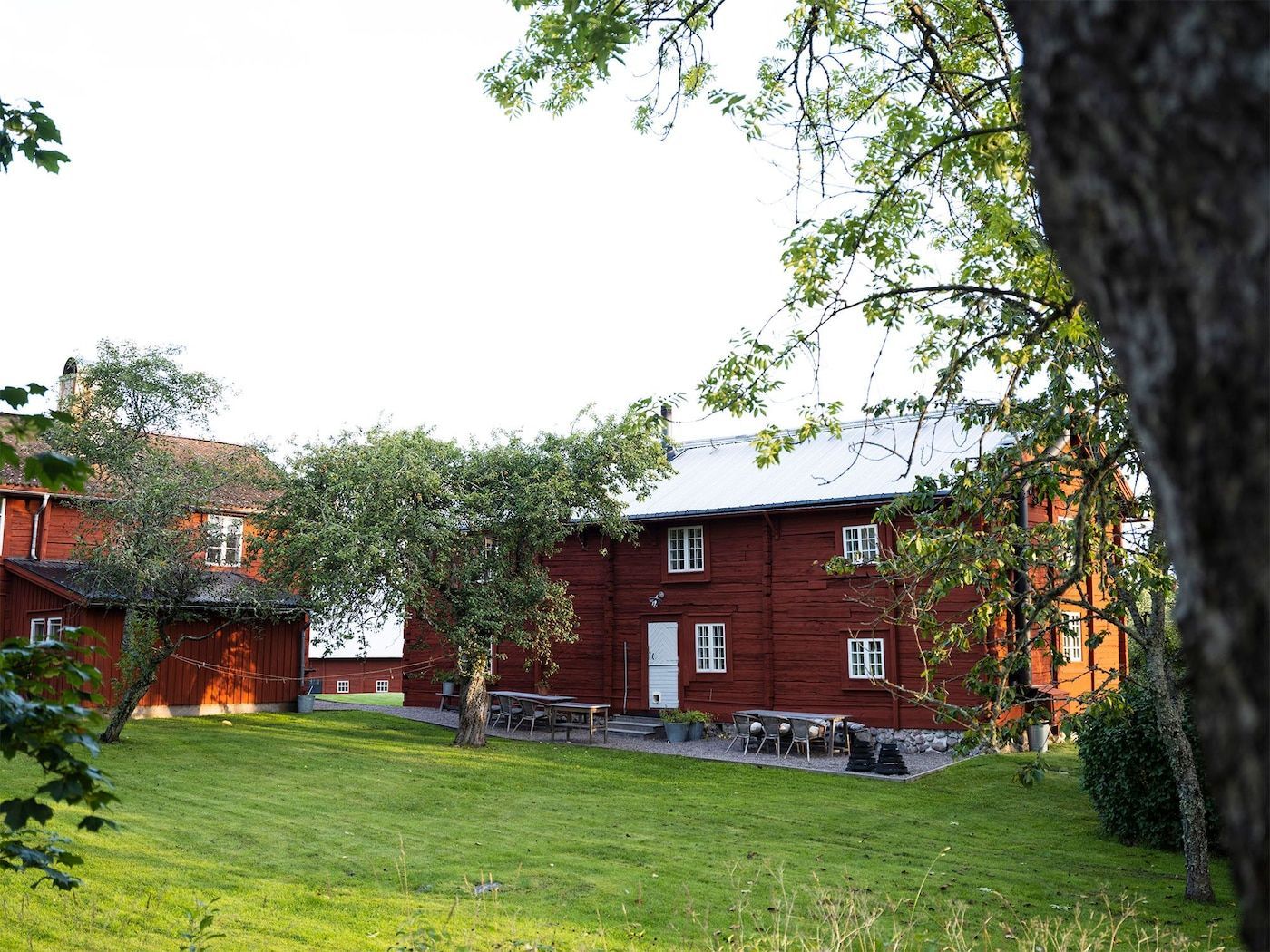 Two red, perpendicular farmhouse buildings looking onto a grassed area.