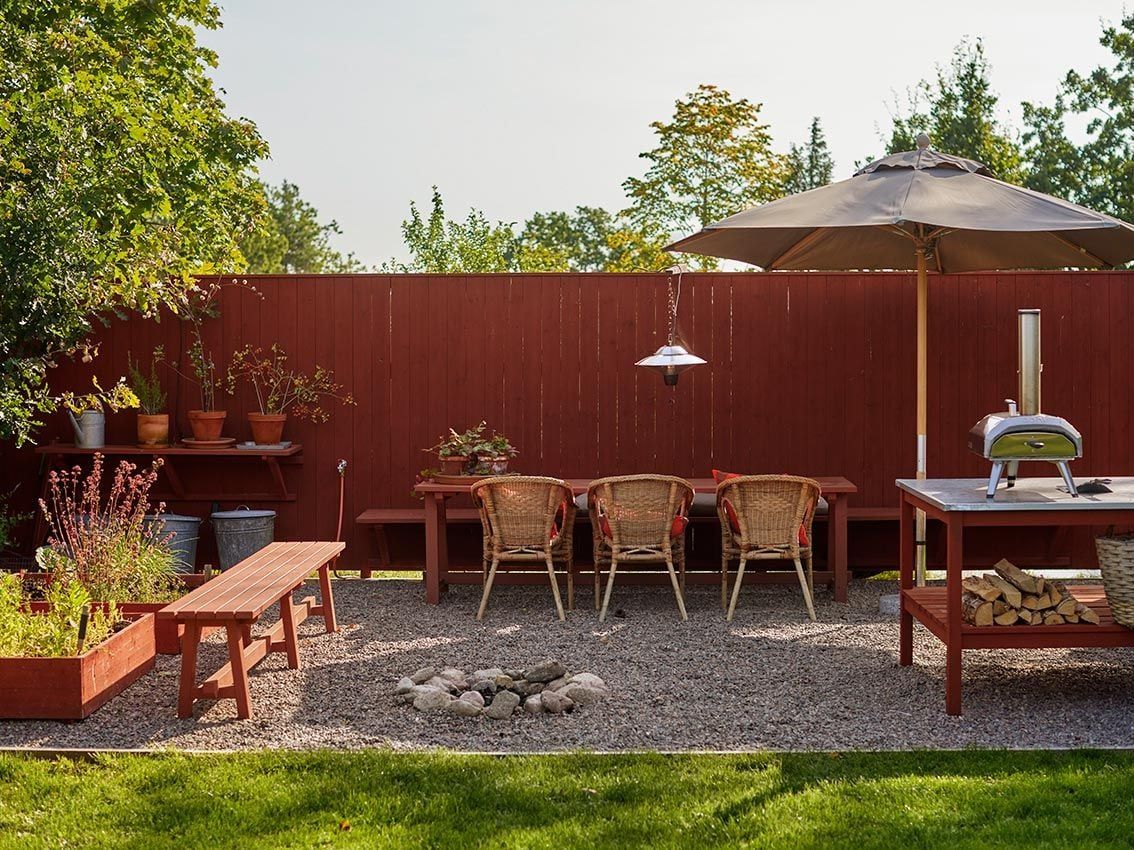 A gravelled outdoor seating area with red-painted screen wall, and open fire pit.