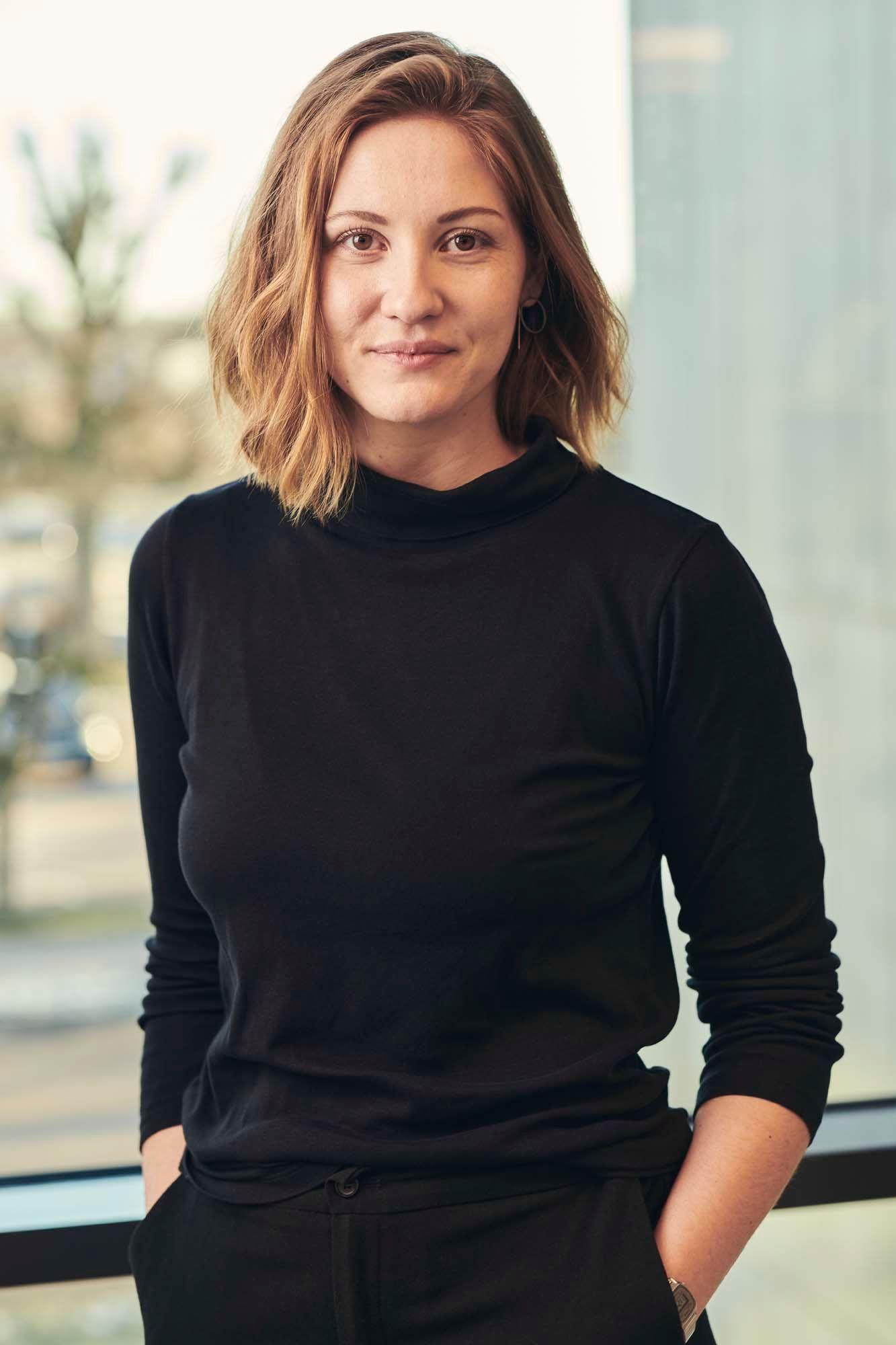 Anna Maria Nilsson stands in front of a window. She is looking at the camera and smiling.