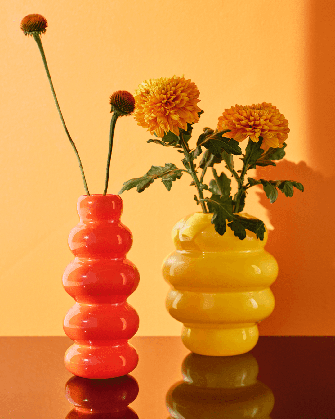 An orange background appears behind the cutout of two KÄLLARHALS vases filled with flowers.