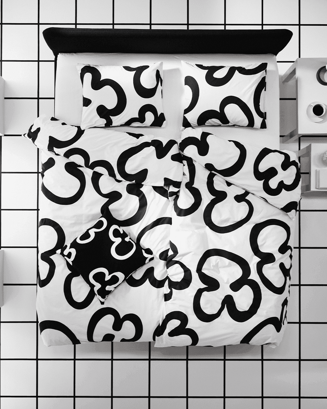 A cutout of a KLIPPBRÄCKA duvet cover and two pillows transforms into an aerial image of the bed linen on a bed, against a black and white windowpane check roomset.