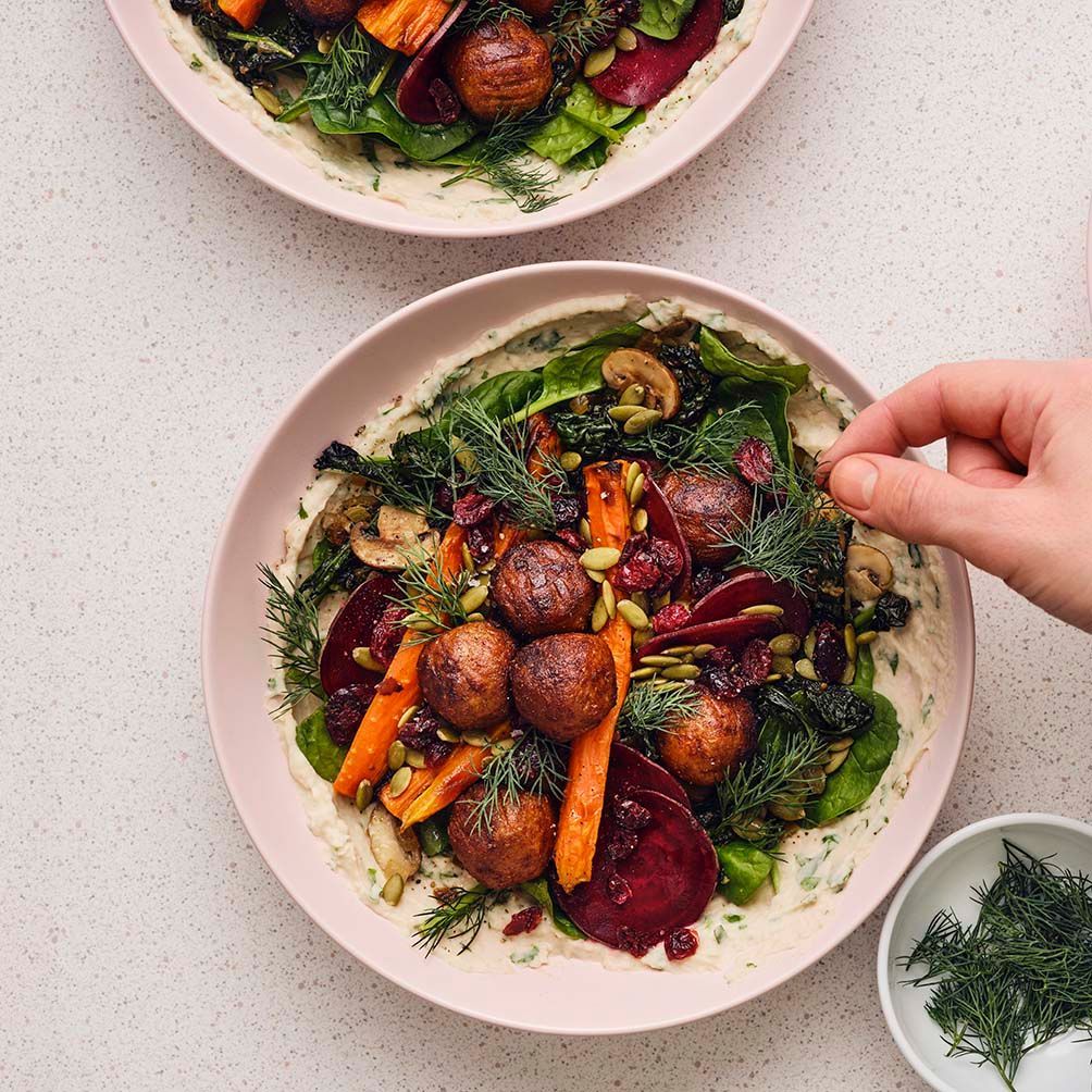 A person adding the garnish to an autumn salad with plant balls and bean dip in a white bowl.