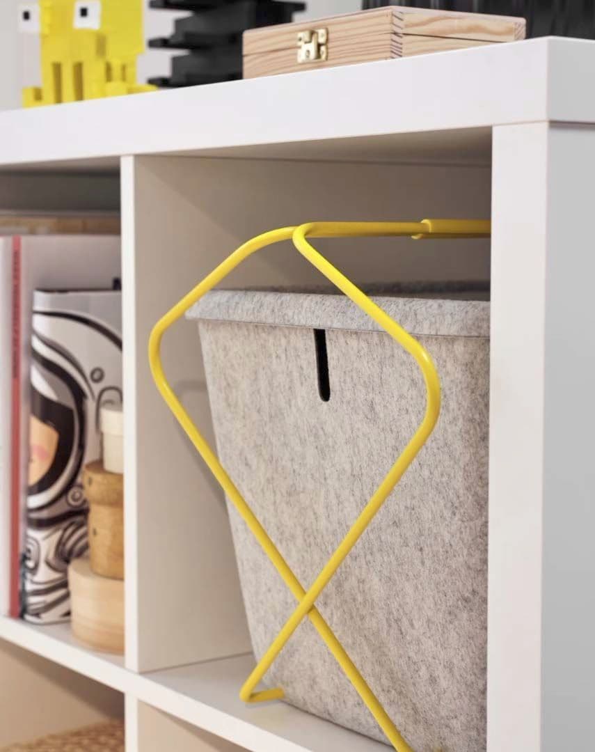 A still image of a grey felt basket with yellow legs from the BRÄNNBOLL gaming collection on a shelf.
