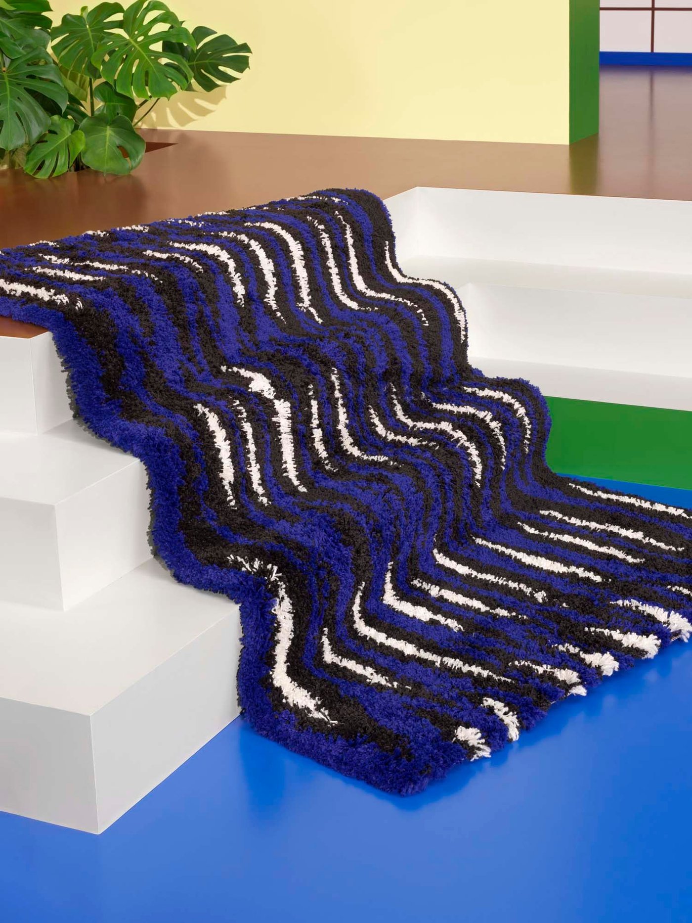 A blue, black and white BULLERREMSA rug is laid out over three steps, at the bottom of the steps is a blue floor.
