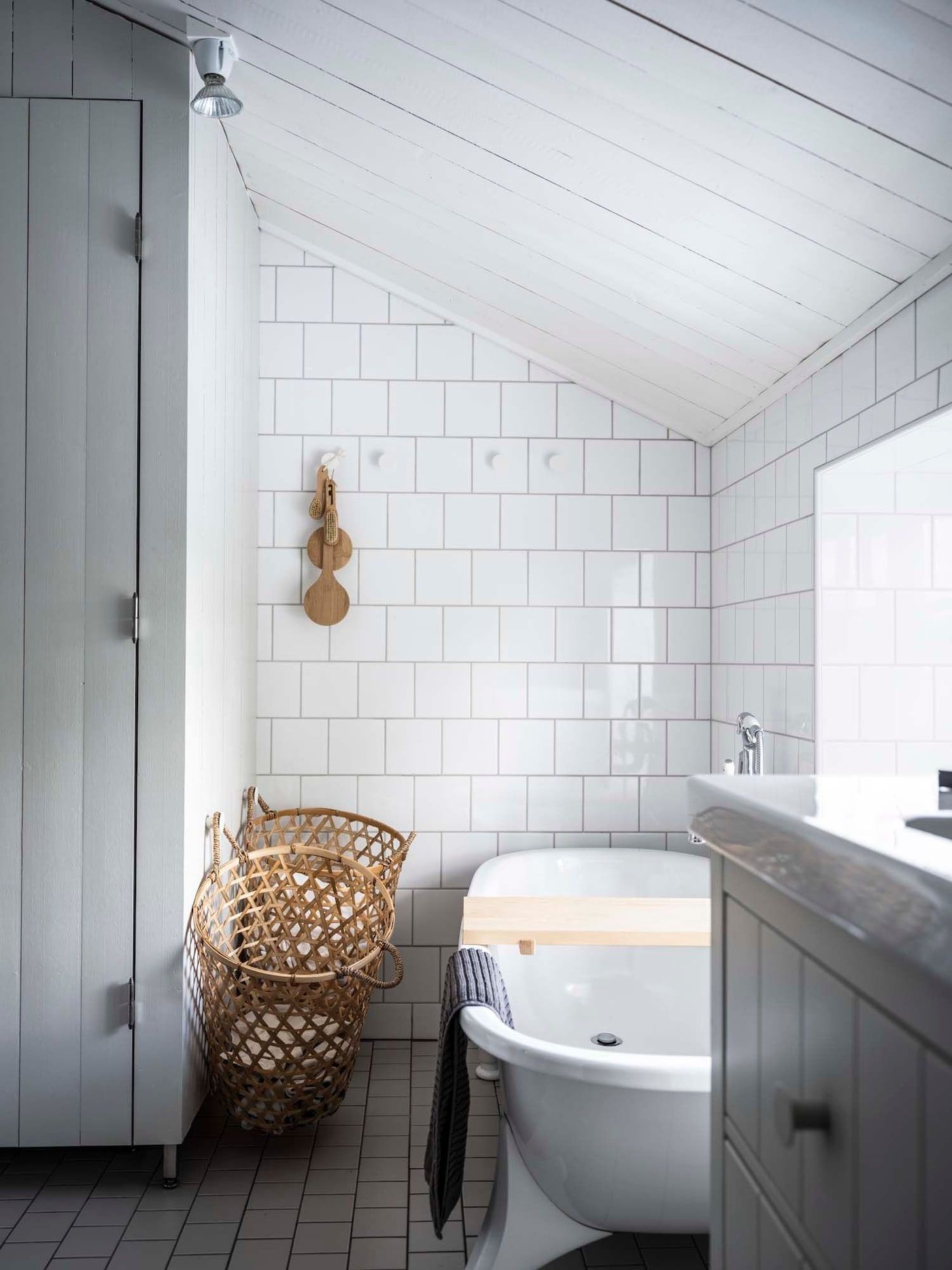 A bathroom with white tiled walls and two woven laundry baskets hanging from hooks
