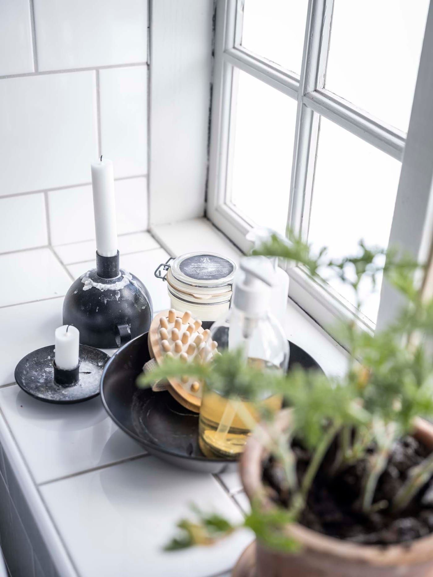 A bathroom windowsill with candles and bath accessories.
