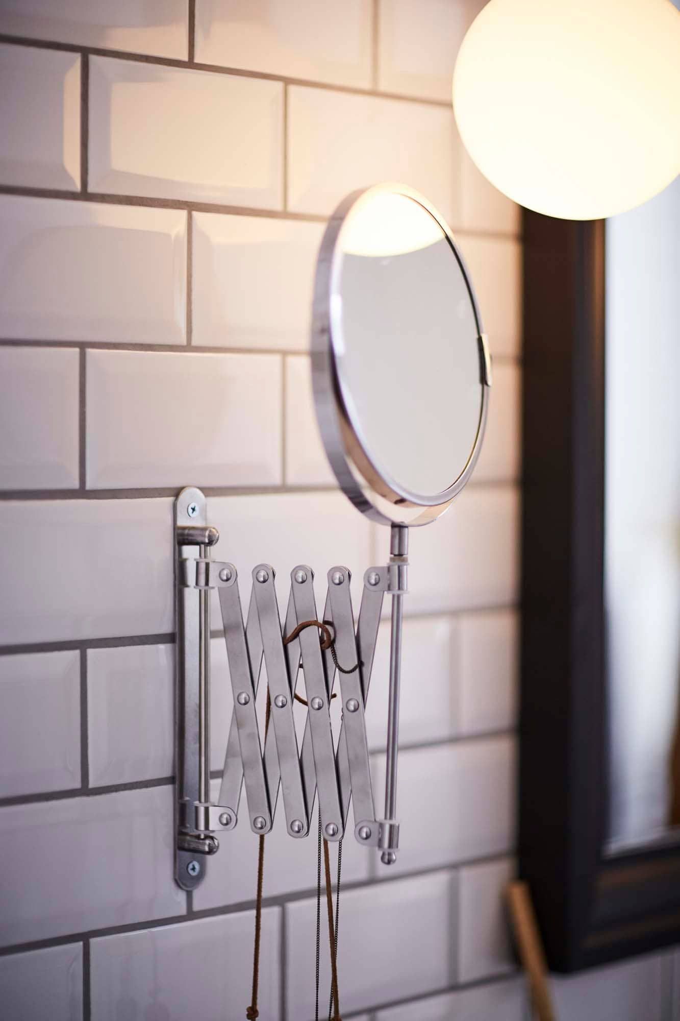 A FRÄCK mirror is attached to a tiled bathroom wall.