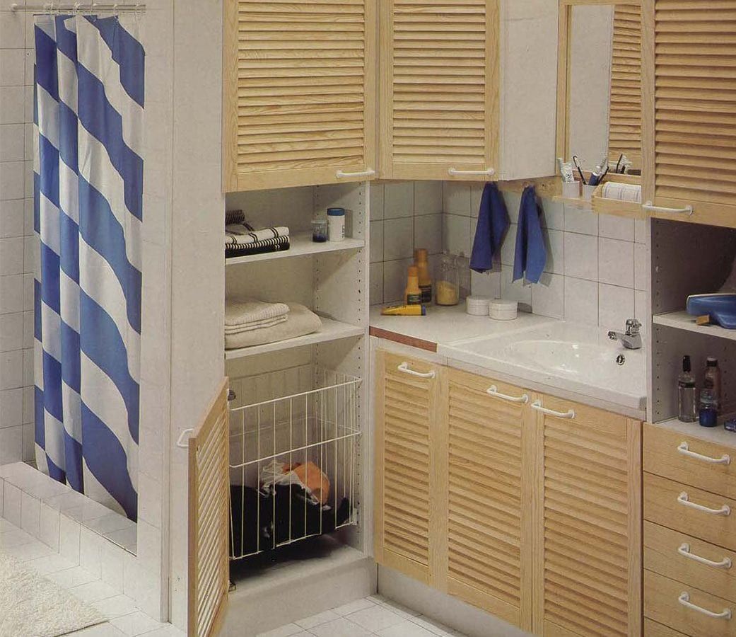 A white bathroom with pine cupboard doors. A door is open, revealing storage.