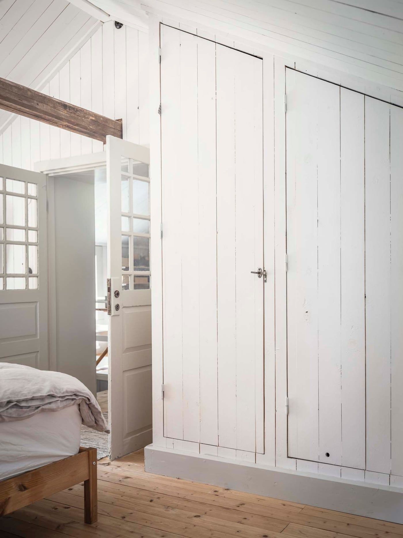Built-in wardrobes with white-painted wooden doors beneath a sloped ceiling in a bedroom.