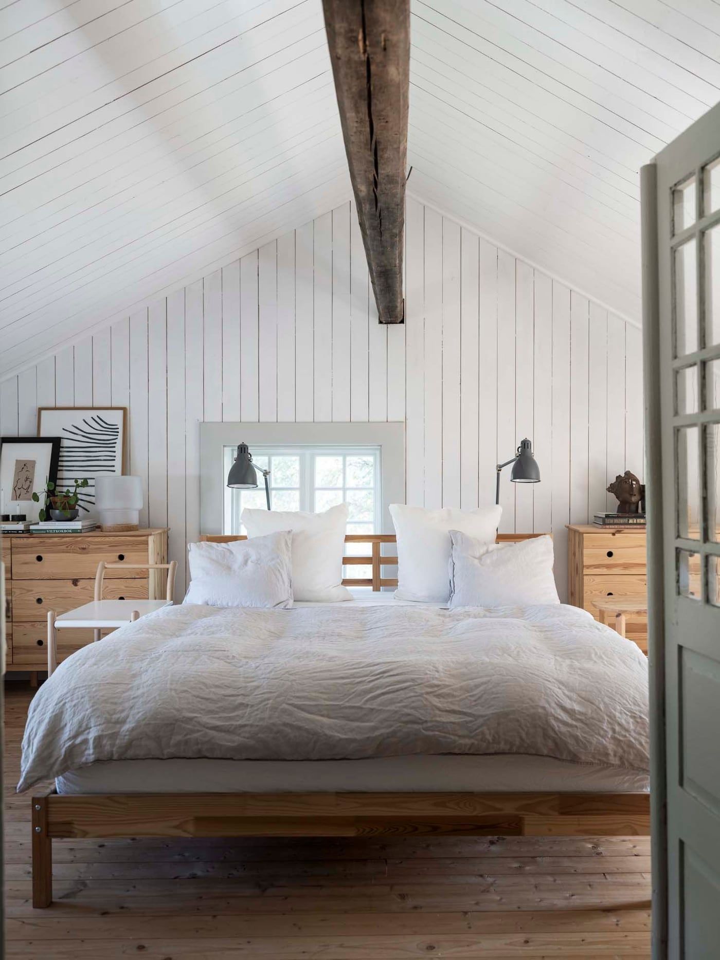 A bed with white bed linen, flanked by two wooden chests of drawers.