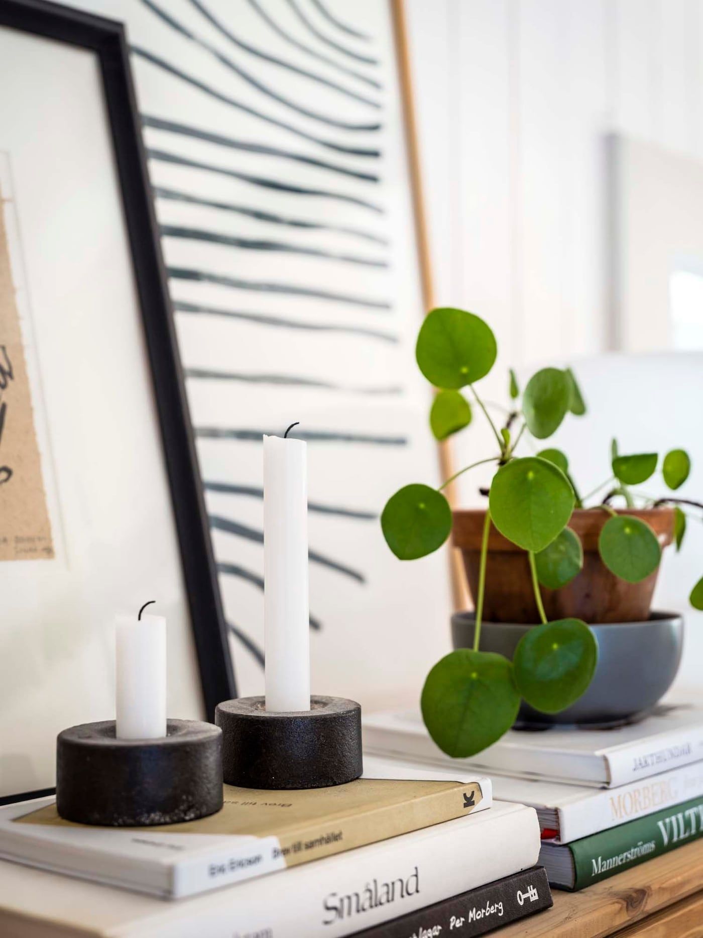 A styled vignette of candles, books, artworks and a pot plant.