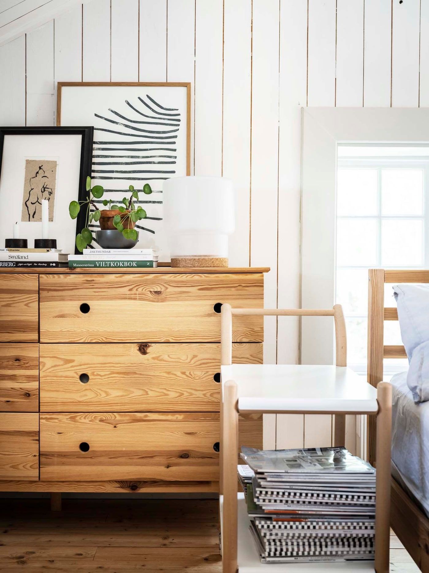 A wooden chest of drawers and two-level trolley with books beside a bed.