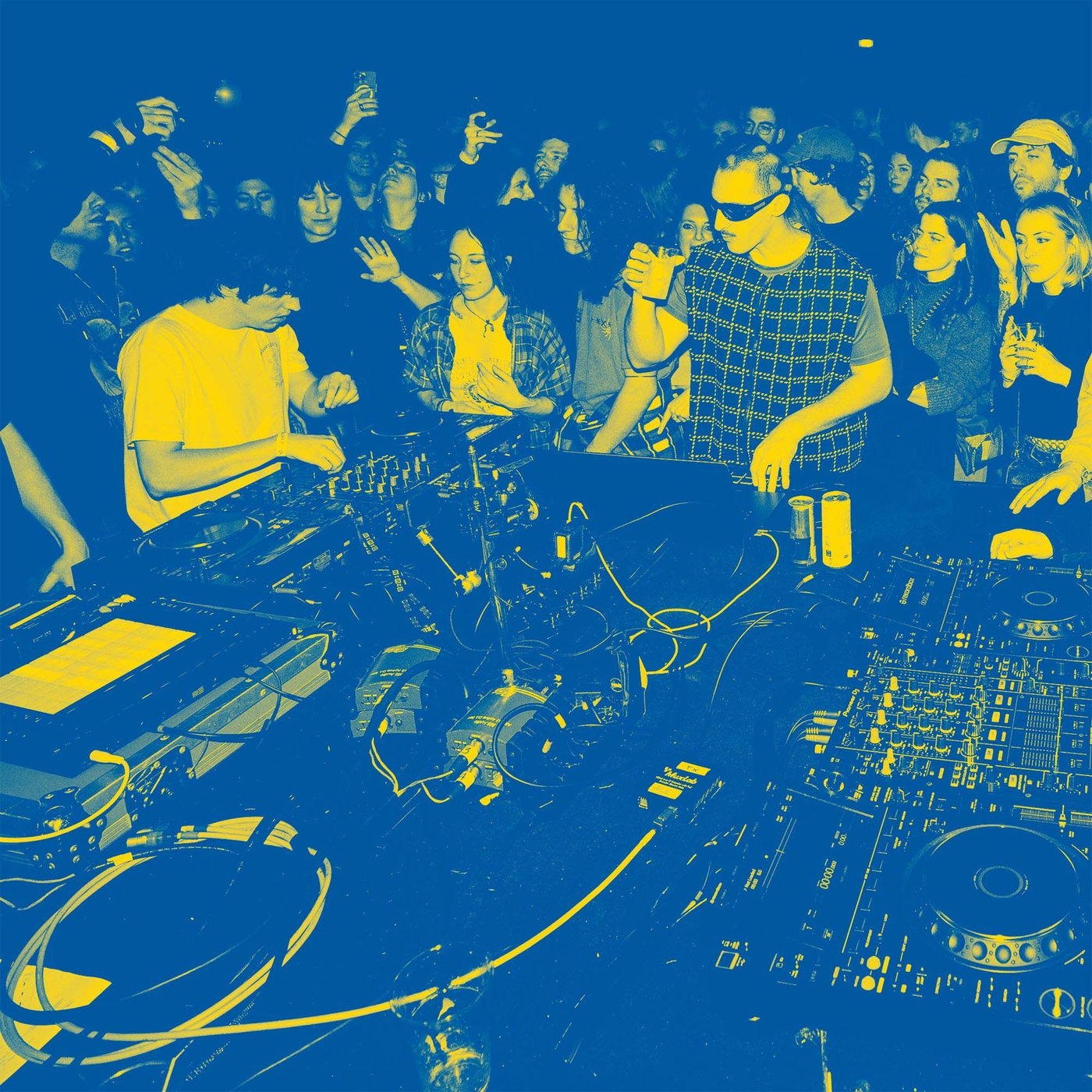 View over the DJs and their setup while playing to a crowded dance floor in a club.