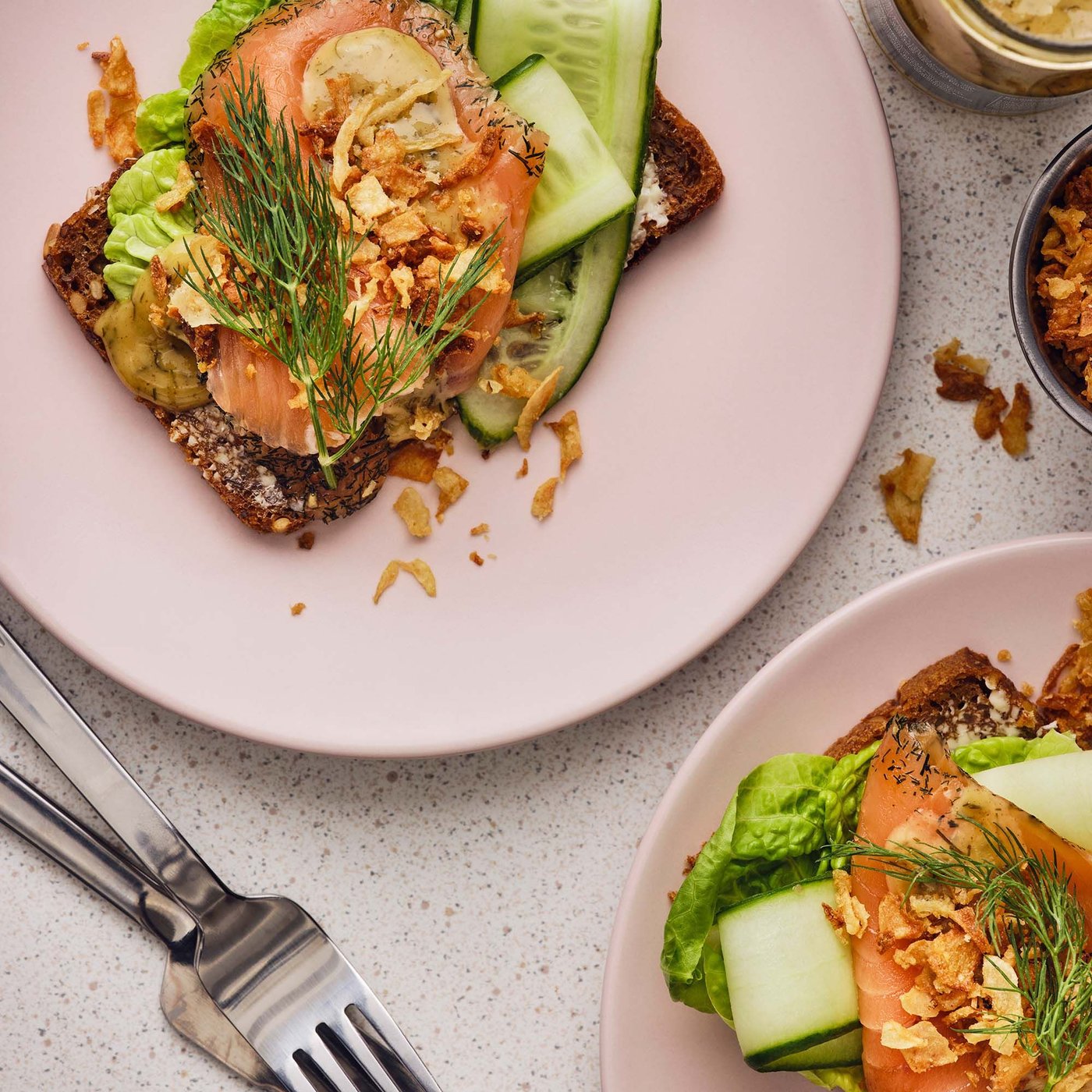 Two IKEA open-faced sandwiches on rye bread with smoked salmon, vegetables and sprinkles of roasted onion.