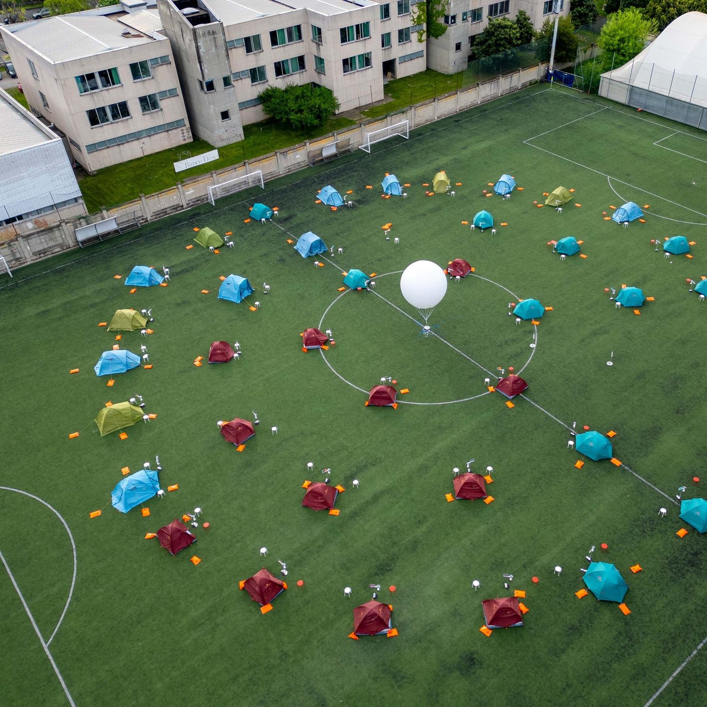 Drone view of colorful tents placed in a circle on a soccer field