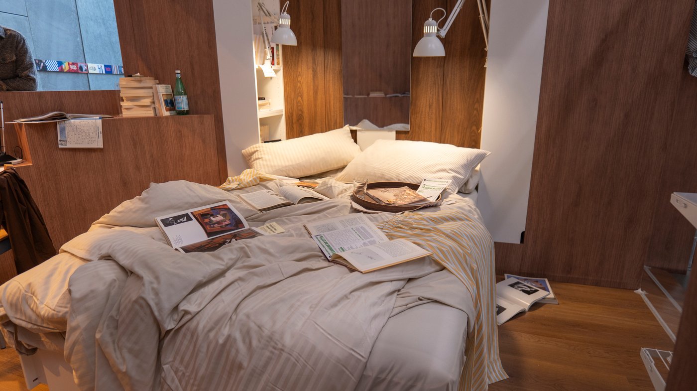 A messy bed in a wood panelled bedroom setting.