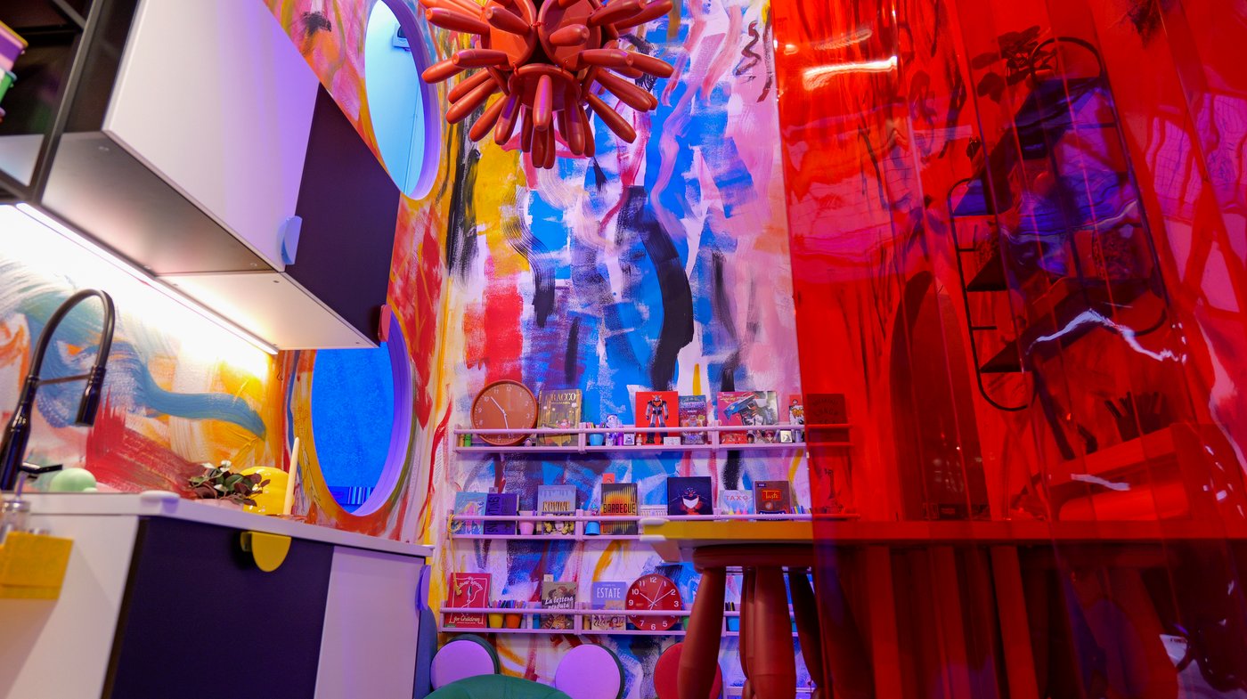 A room with colourful, hand-painted walls and a cluster of red MAMMUT stools hanging from the ceiling.
