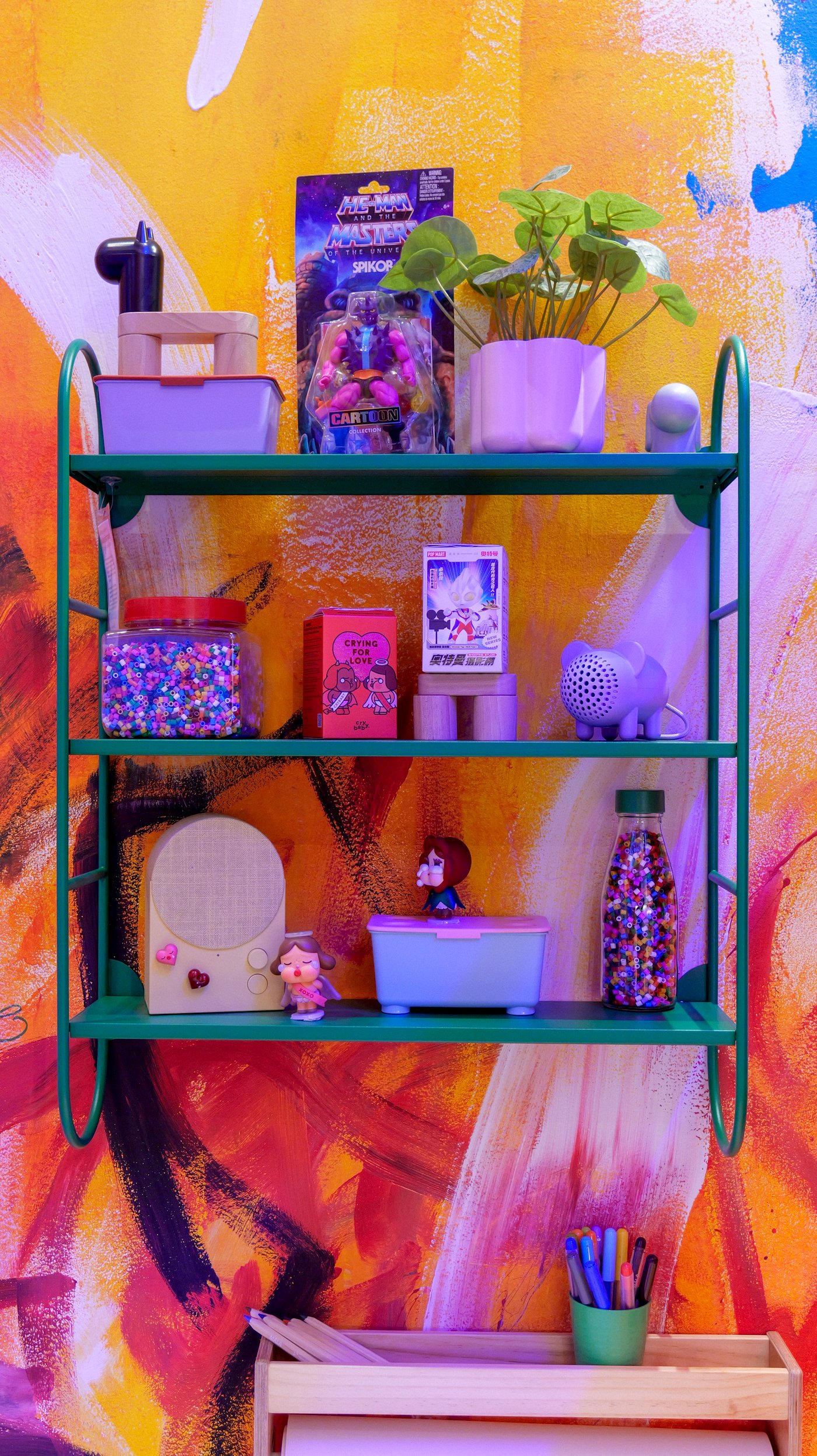 Objects on a green FÄRGSÄTTARE wall shelf against a colourful, hand-painted wall.