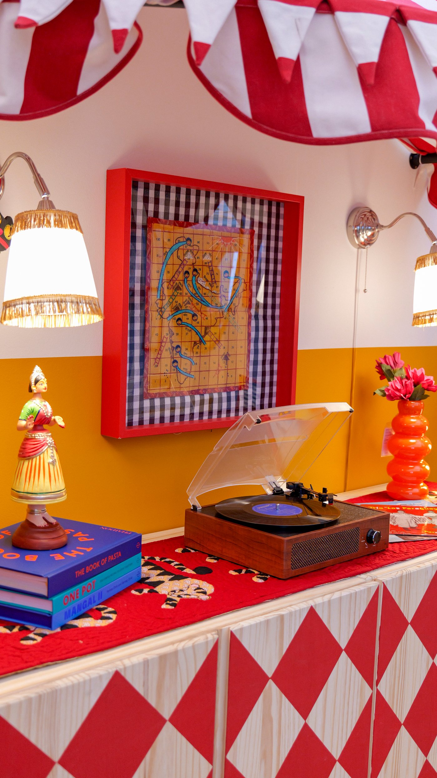 A red-framed image hangs on a colourful two tone wall, above a record player on a red and white table.