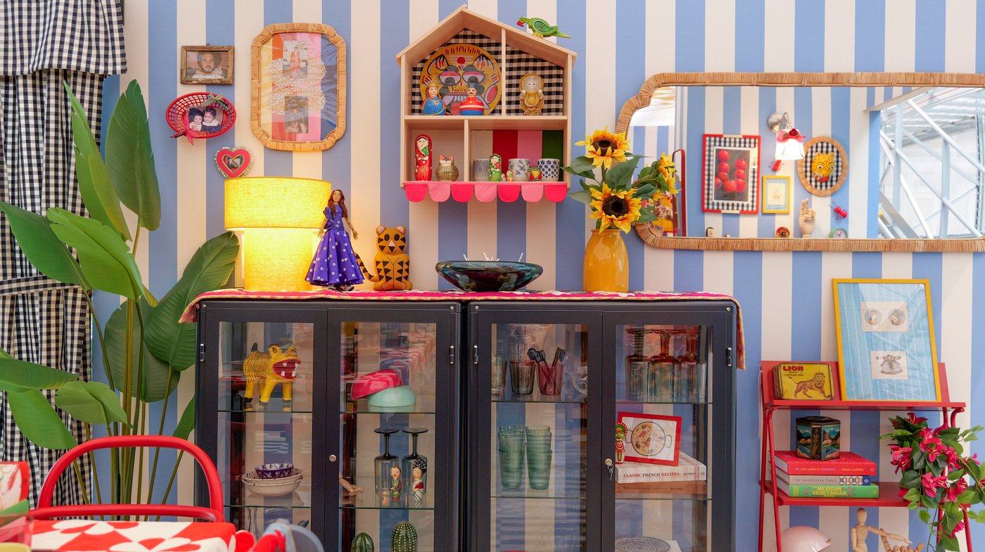 A blue glass-fronted cabinet filled with and surrounded by decorative objects against a blue and white striped wall.