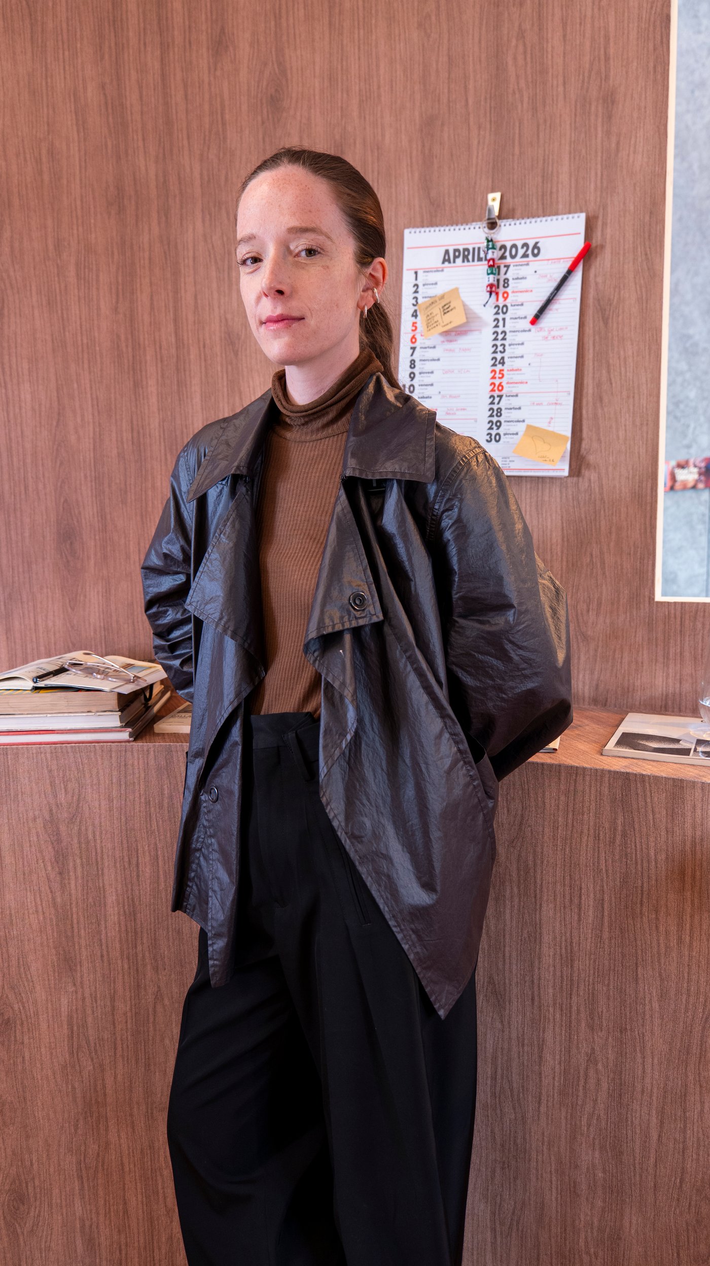 Charlotte Taylor stands in front of a curved wood panelled wall and leans against a shelf with books.