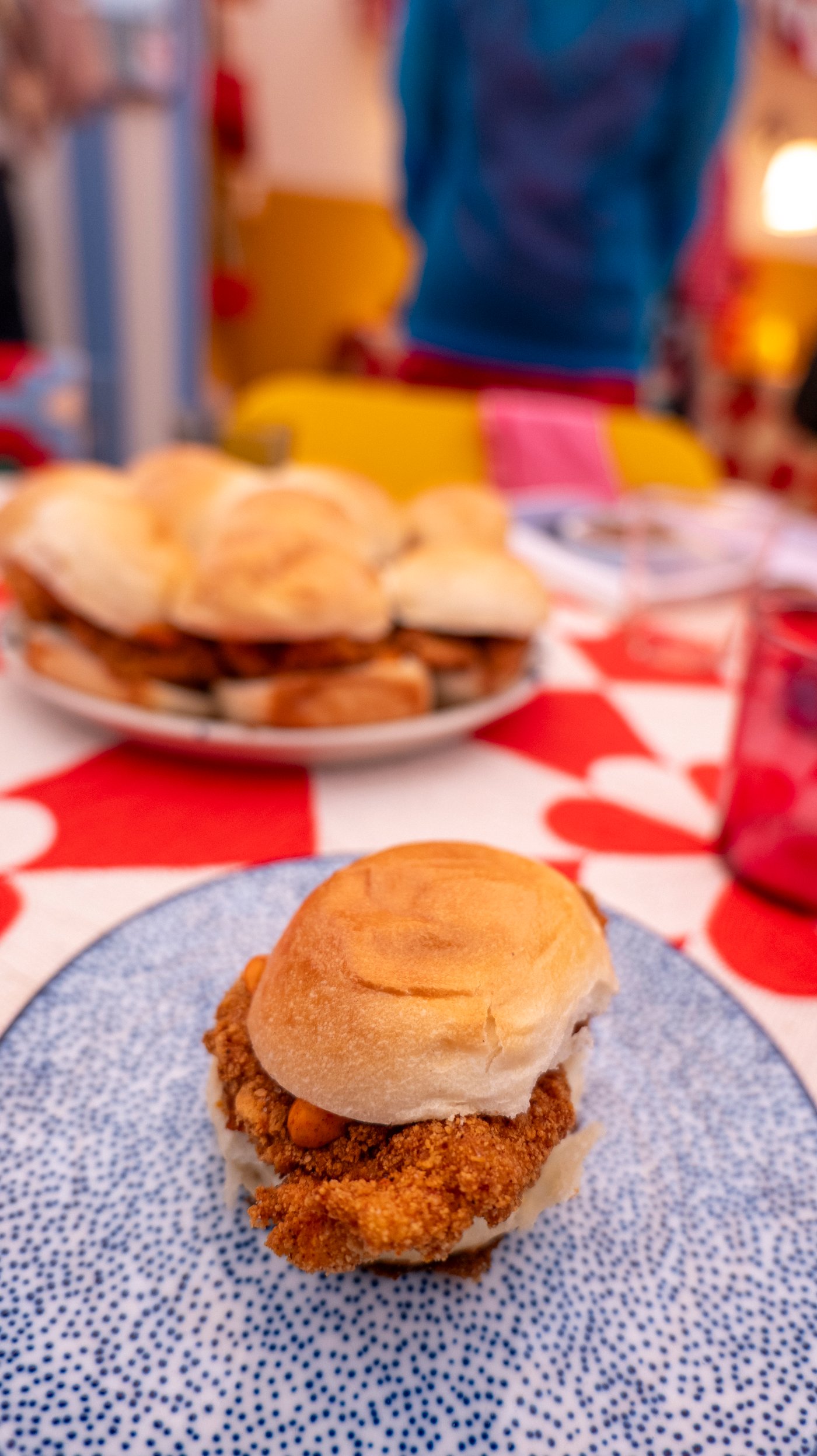 A chicken burger on a blue and white patterned plate, sits on a red and white patterned dining table.
