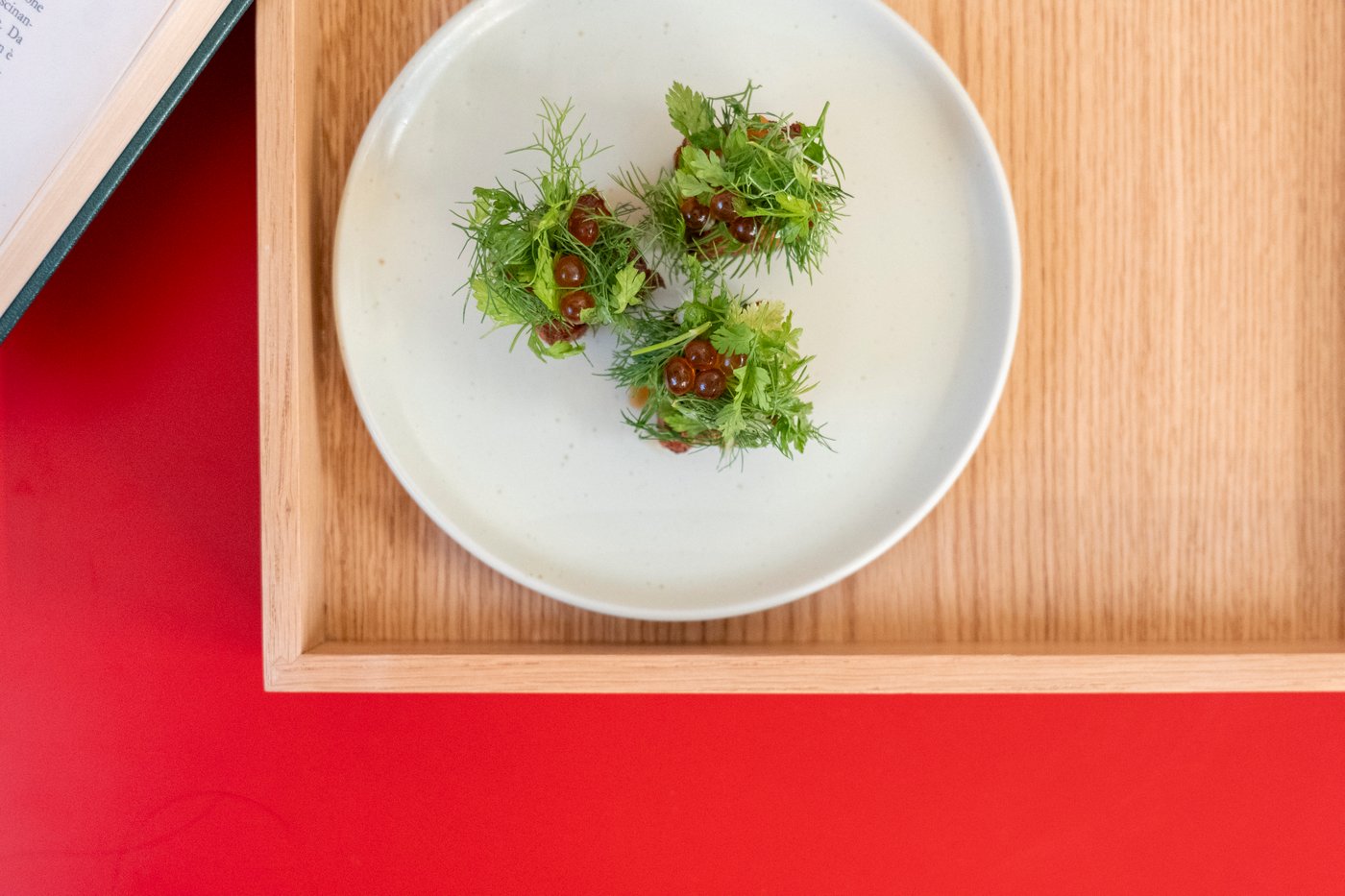 An aerial view of three garnished kimchi rice bites on a plate and wooden tray, on a red surface.