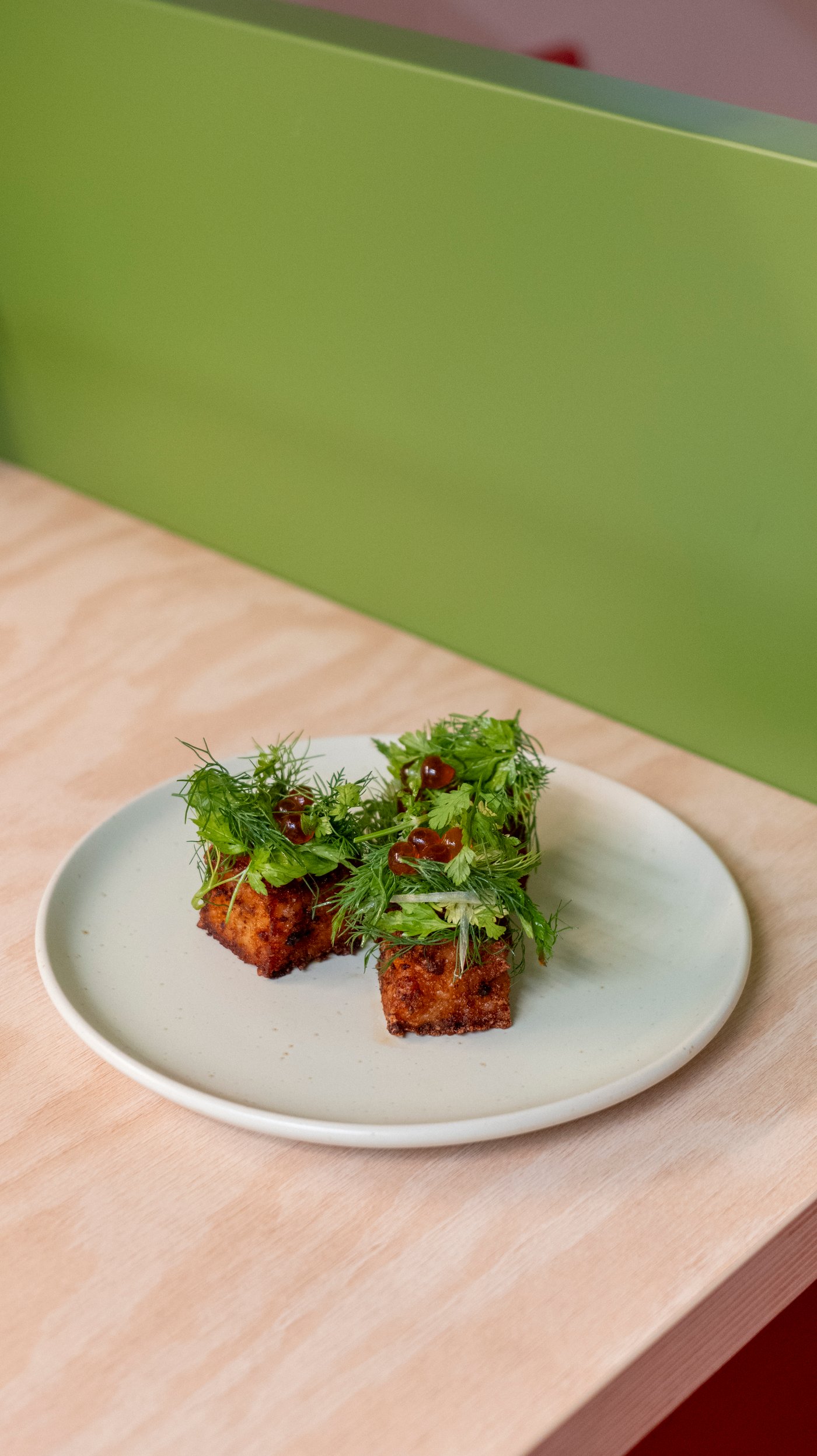 The corner of a wood table with a plate containing three kimchi rice bites on a plate.