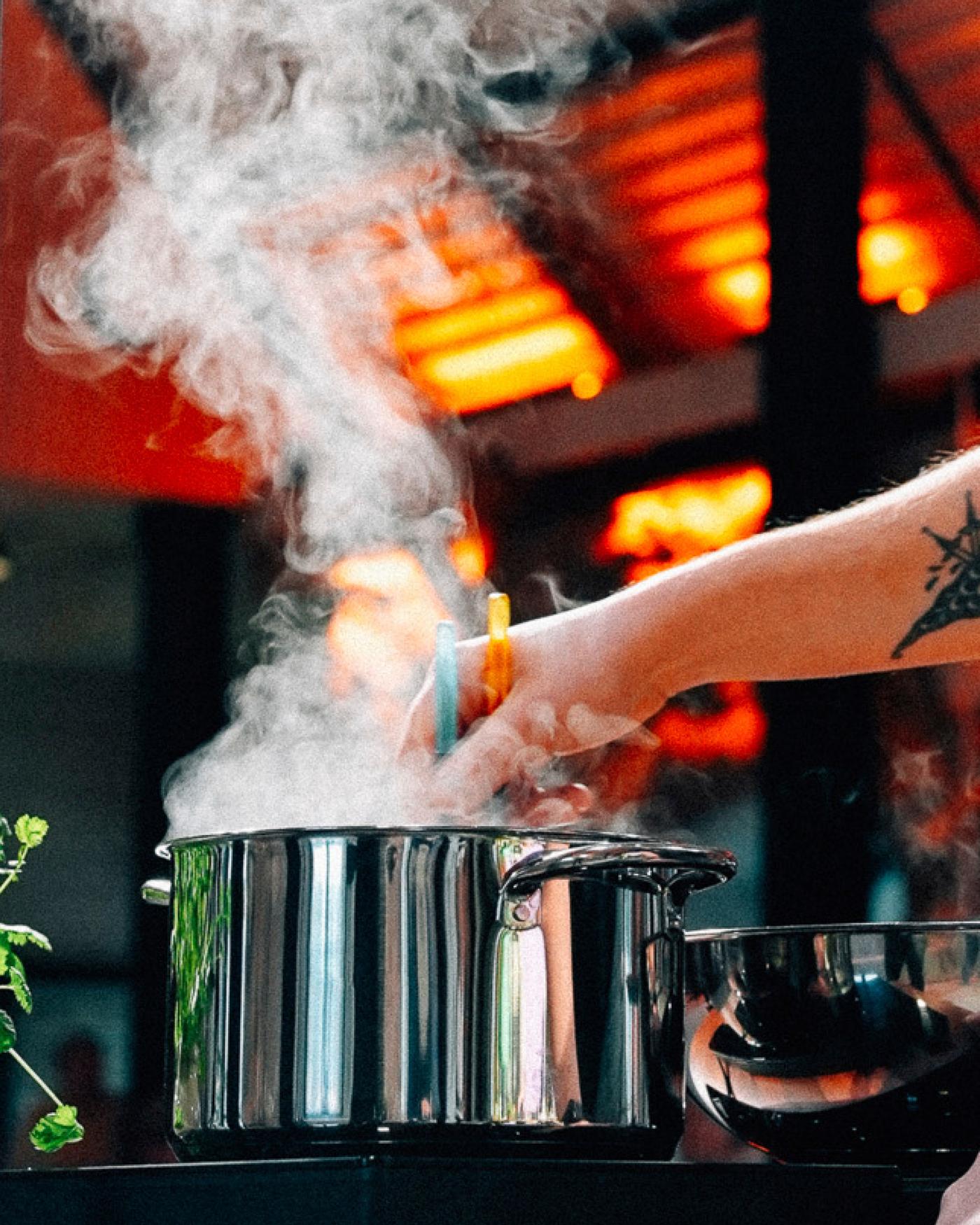 A hand stirs a boiling pot with steam rising.