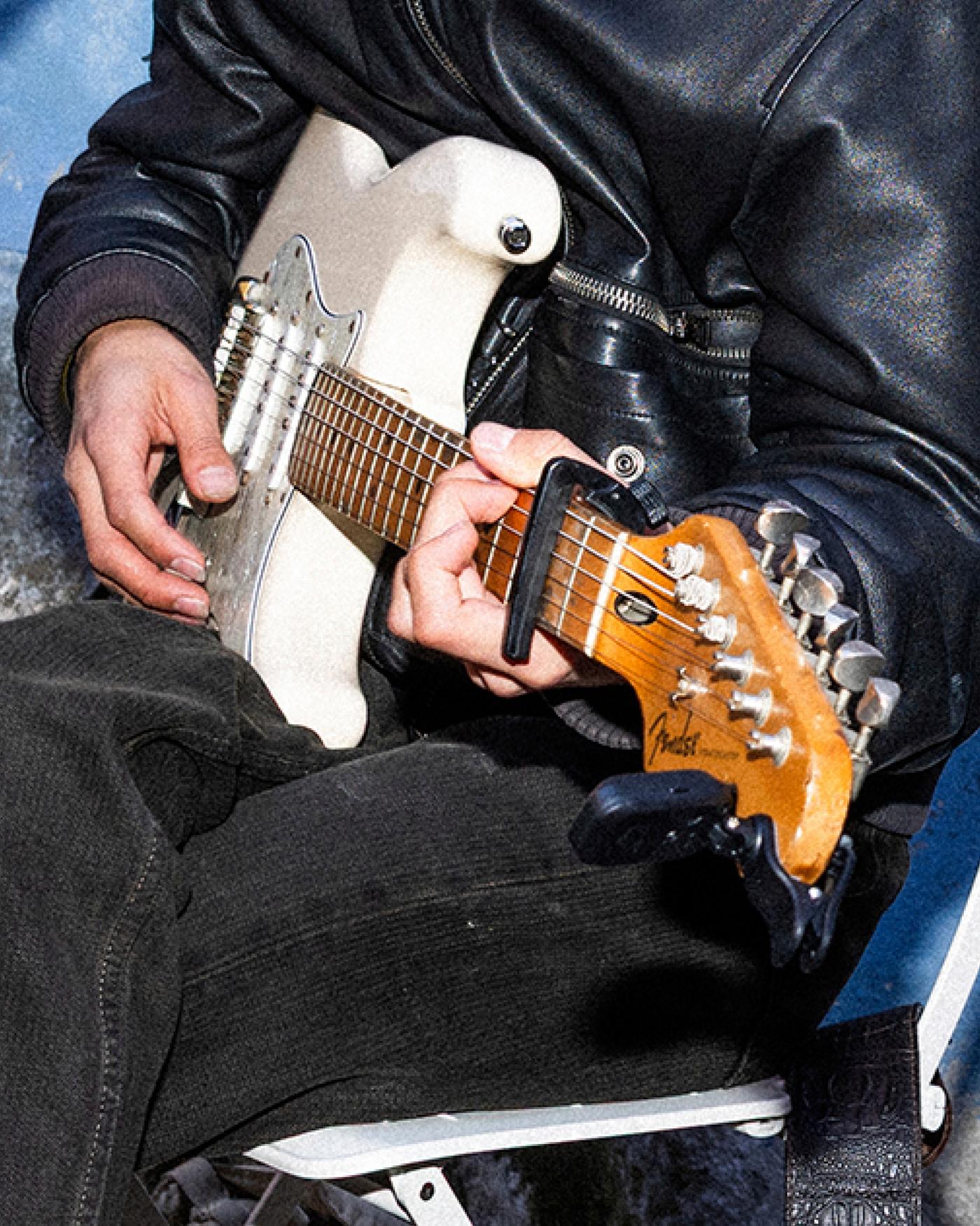a pair of hands play a white electric guitar.