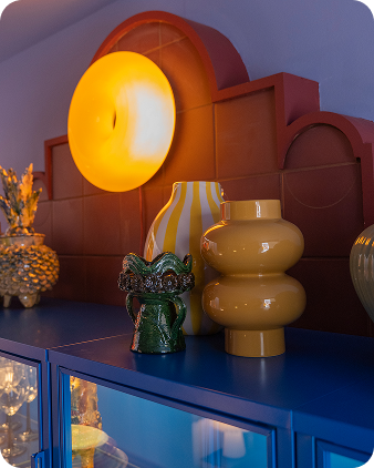 A blue glass-front storage unit with vases and an illuminated lamp on top.