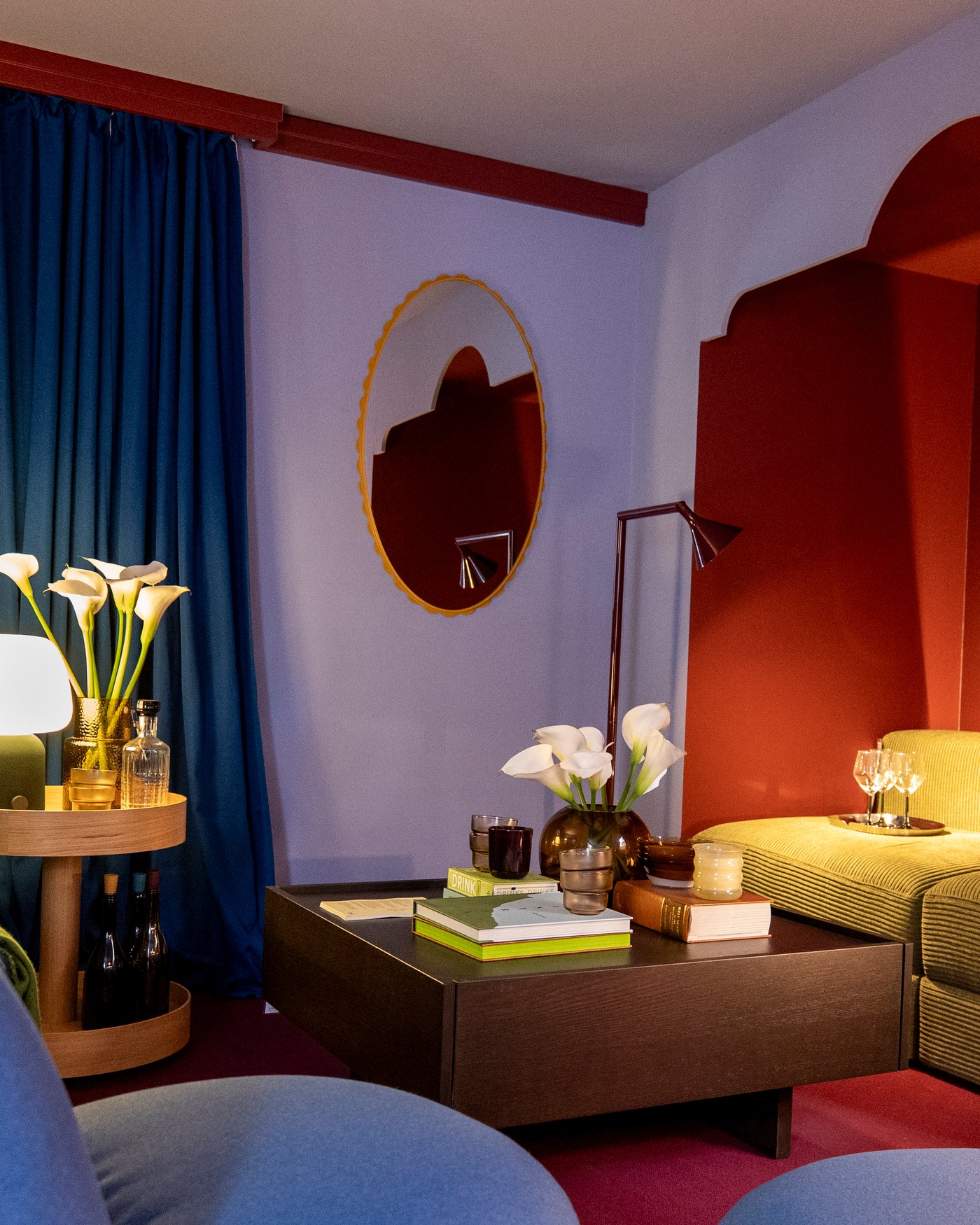 A colourful, moody living room with dark blue curtains, lilac and deep red walls and a dark wood dining table in the centre.