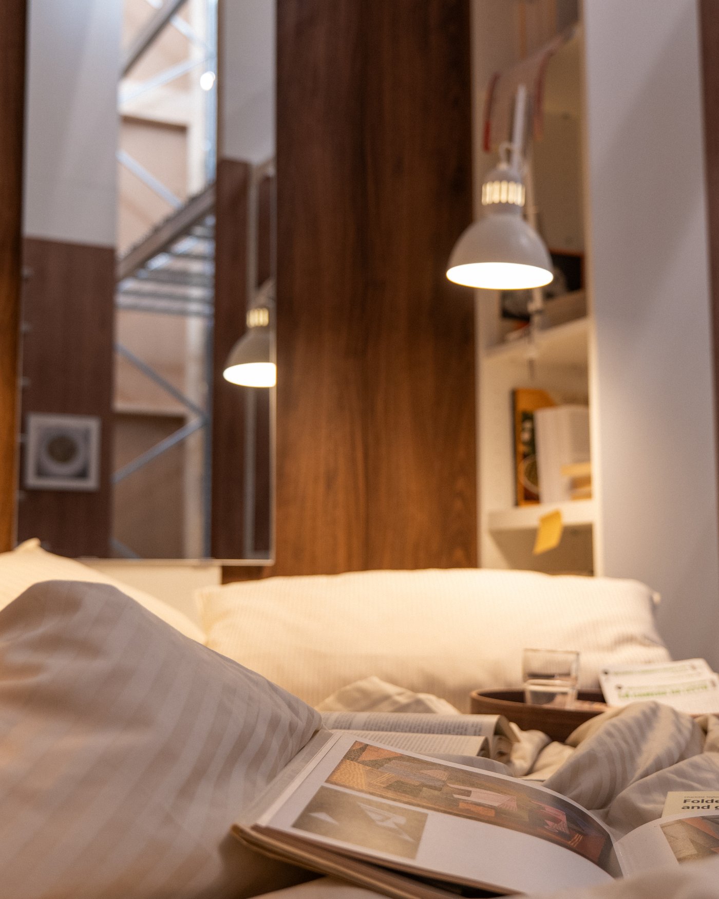 A bedroom with light bedlinen and an illuminated lamp above the bed.