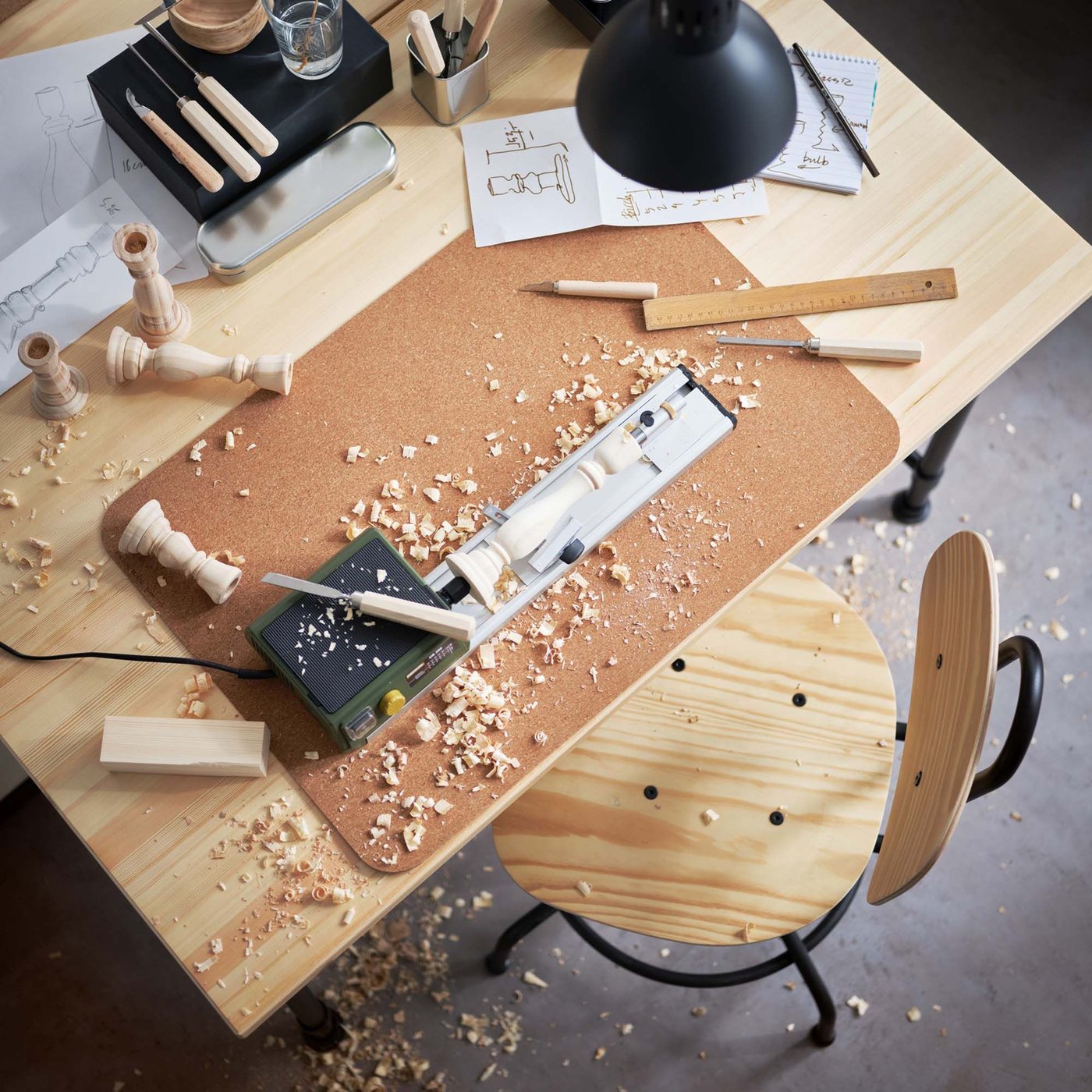 An aerial view of a work table with a benchtop wood lathe, candlesticks and sawdust