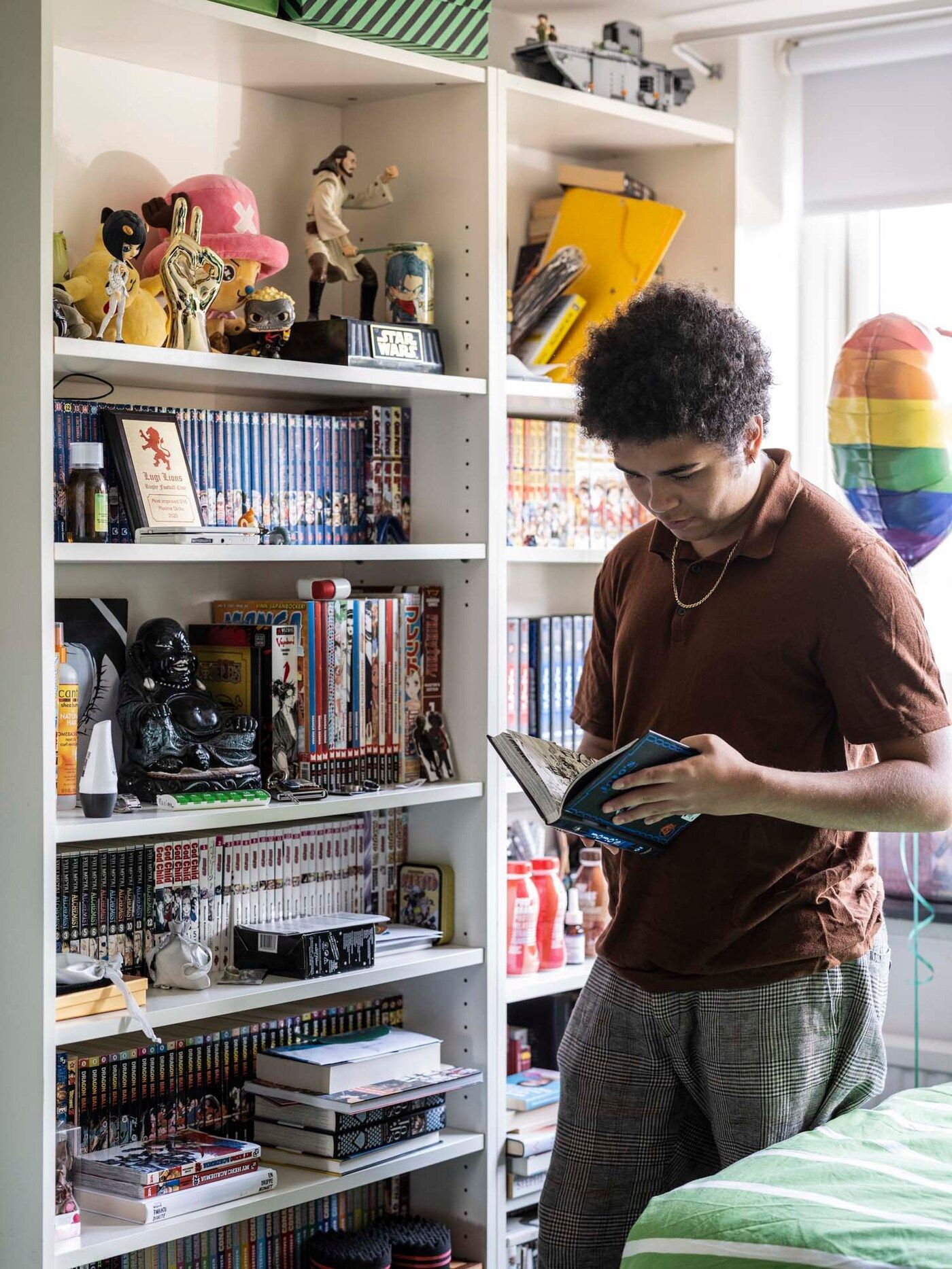Maxime in his bedroom reading a book in front of his bookshelf.