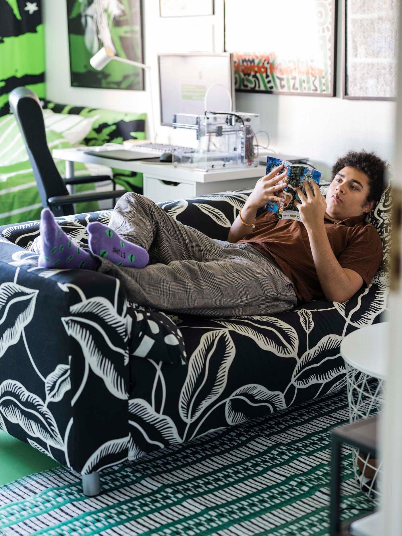 Maxime laying on a black and white graphic sofa, reading a book.