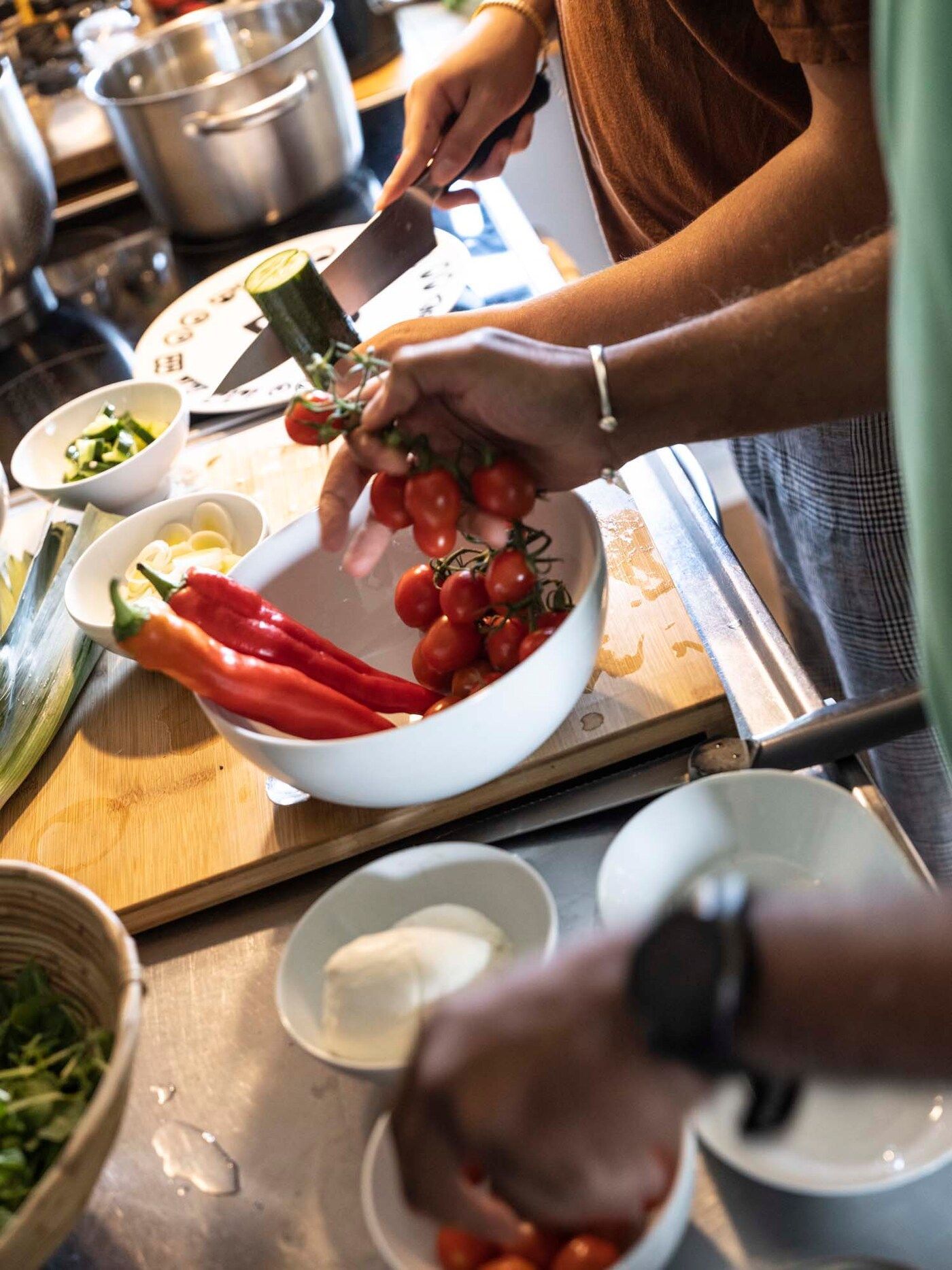 Maxime and Cedric's hands preparing cucumber, tomatoes and peppers for salad.