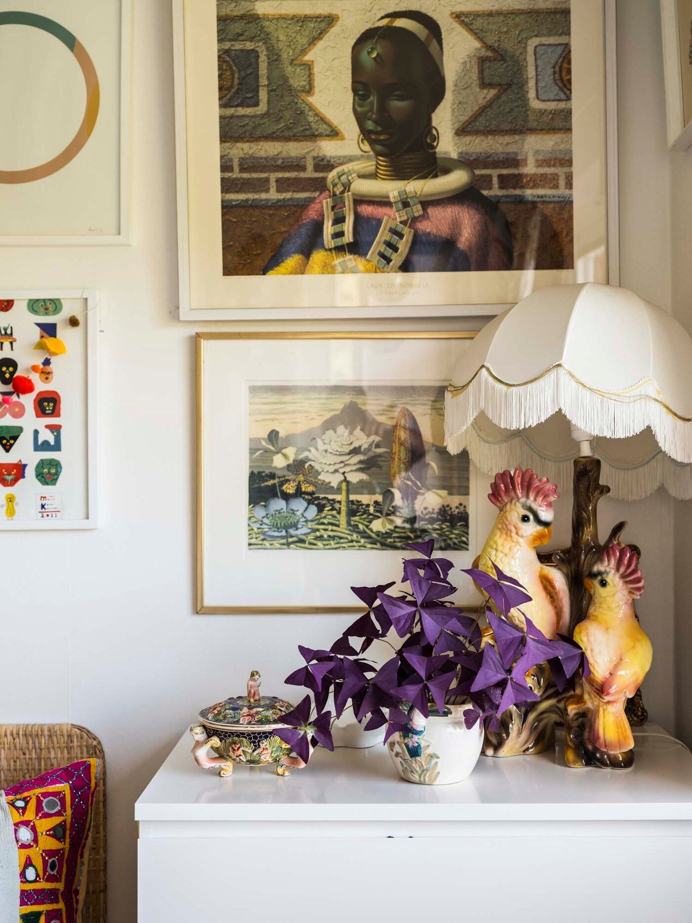 The bedside table in Cecilia and Cédric's room features a bird lamp and a plant. There are pictures on the wall behind.