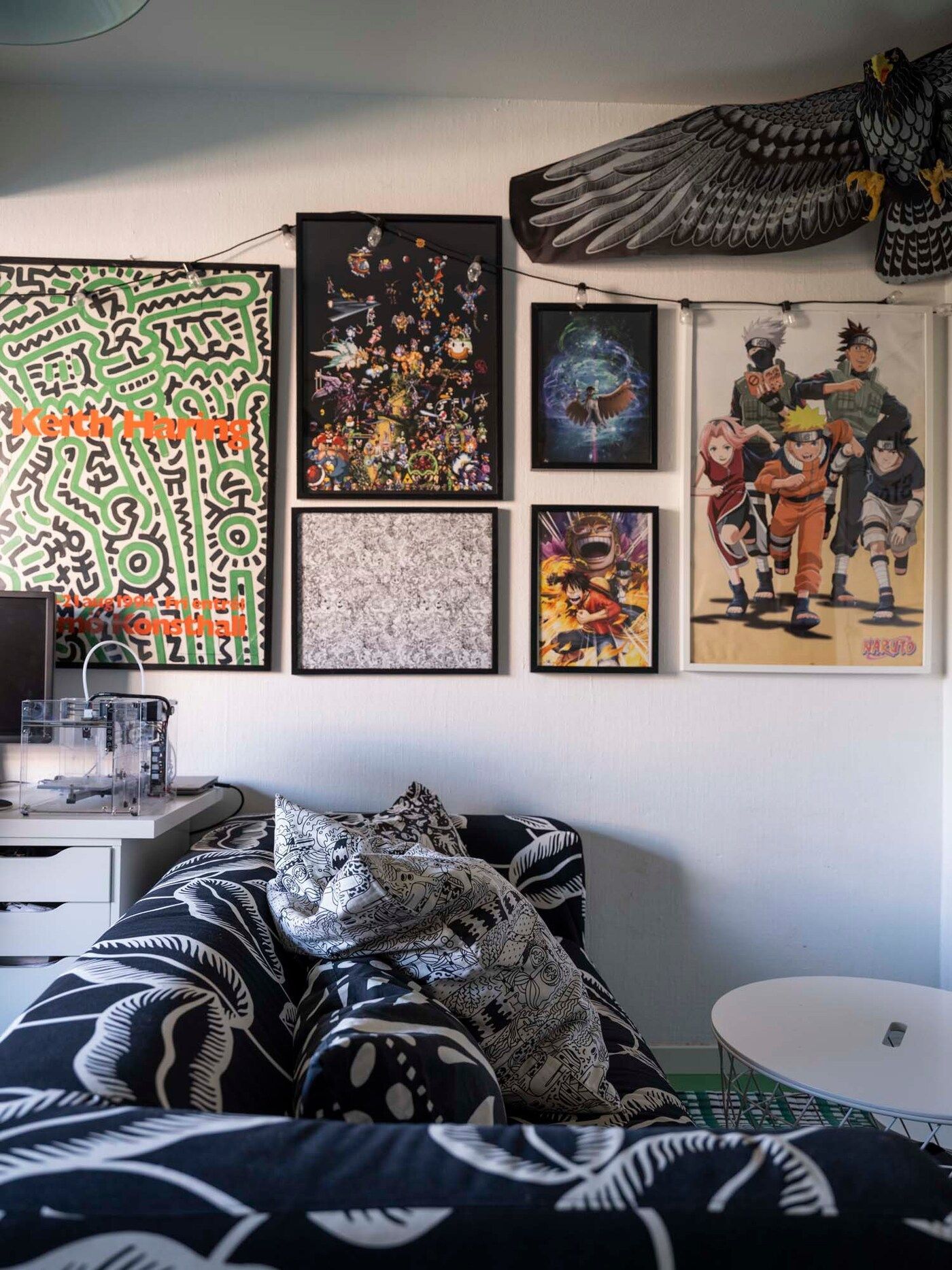 Pictures of manga characters and Keith Haring art hang on the wall, with a black and white sofa in the foreground.