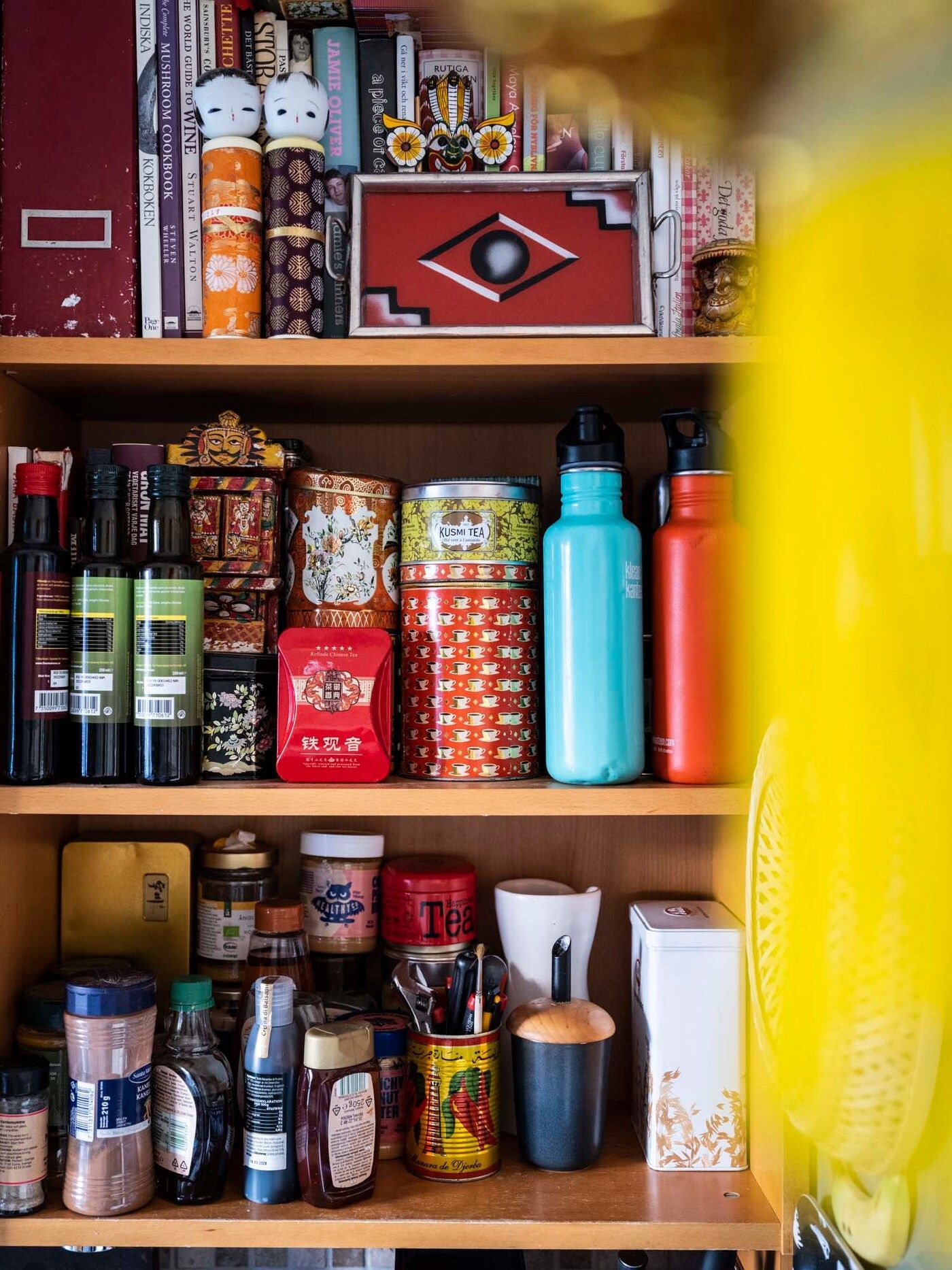 A kitchen cupboard filled with bottles, tins and objects.
