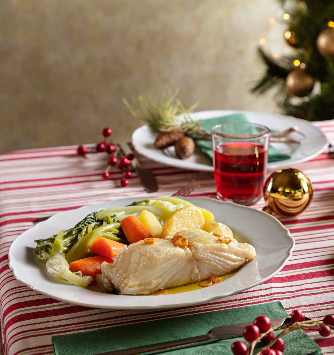Two plates with cod and vegetables sit on a festive table with a striped tablecloth.