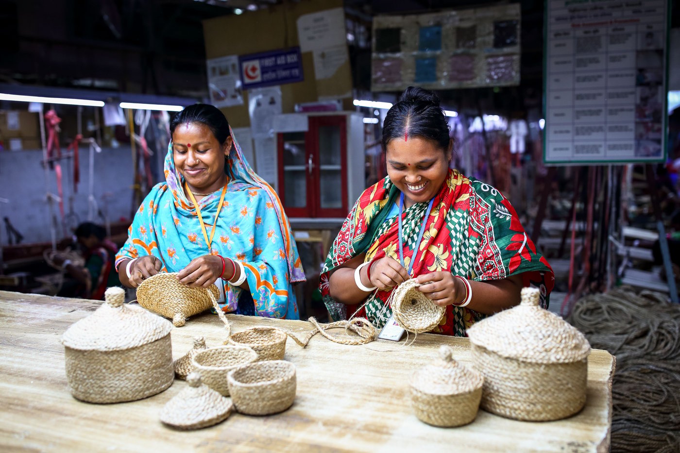 Two woman in colorful clothing braiding baskets