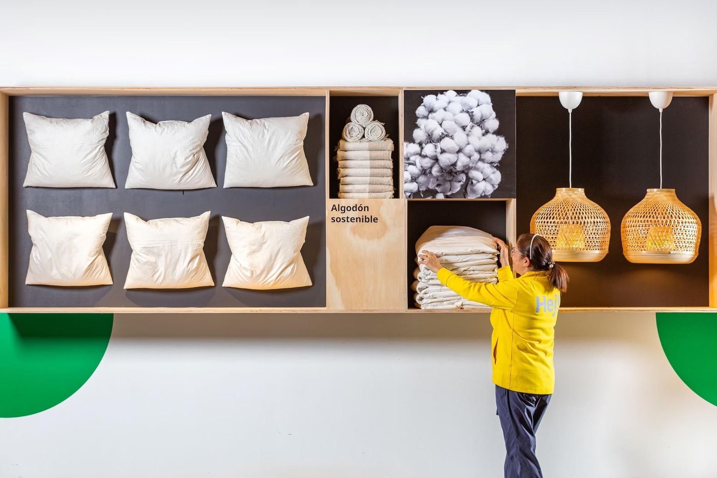 A showroom wall with pillows, lamps, towels and blankets displayed on it. A co-worker putting everything into place, making sure it looks neat.