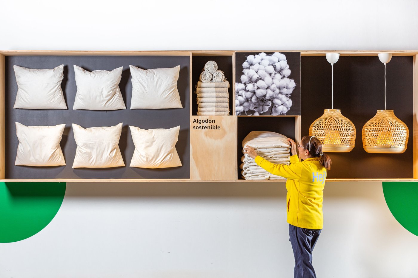 A showroom wall with pillows, lamps, towels and blankets displayed on it. A co-worker putting everything into place, making sure it looks neat.