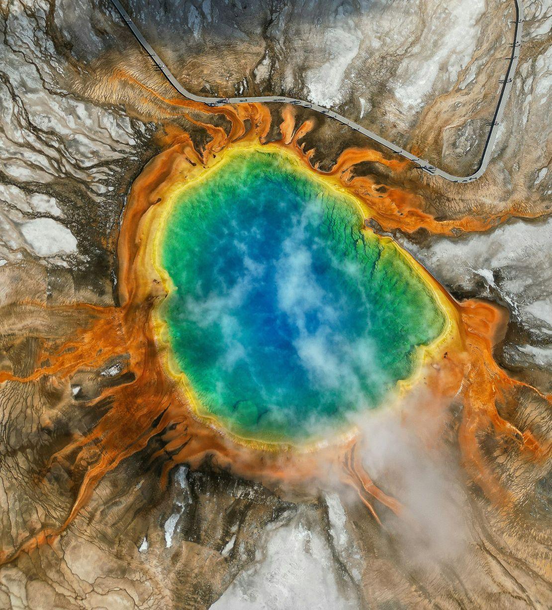 An overhead shot of an almost circular lake in a crater. The blue water is rimmed with yellow and orange earth.